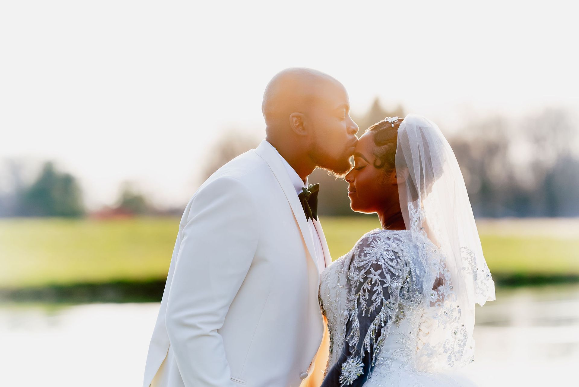 A bride and groom are kissing in front of a lake.