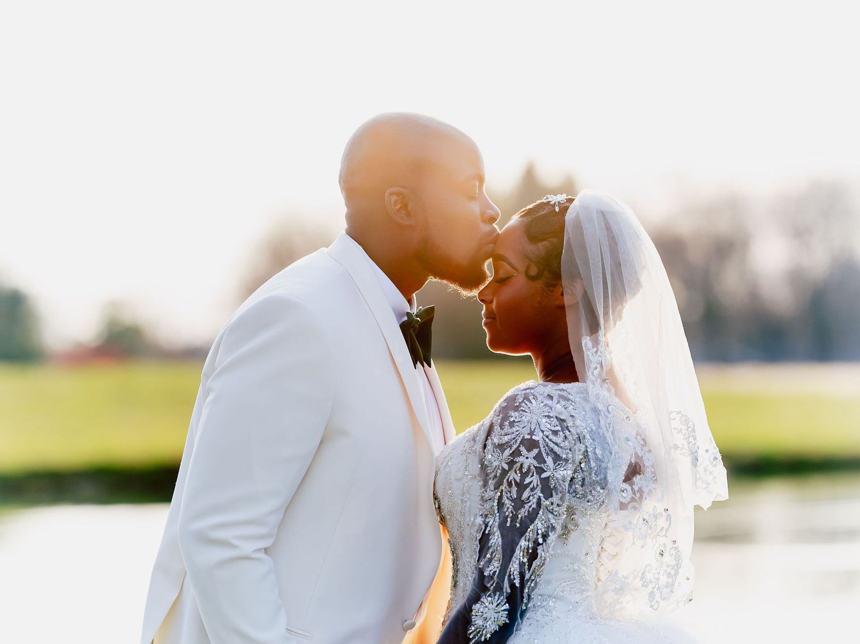 Bride and groom in white embrace and kiss outdoors at sunset