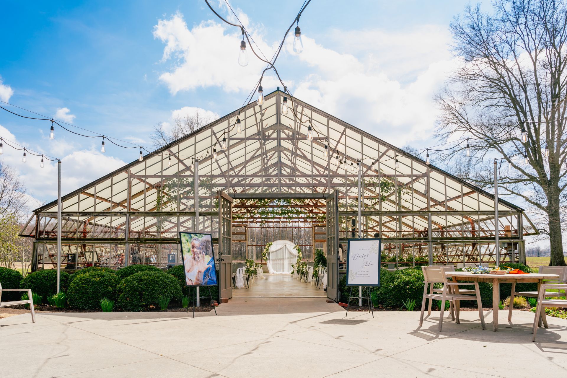 Glass greenhouse entrance with a white archway, under a blue sky with clouds