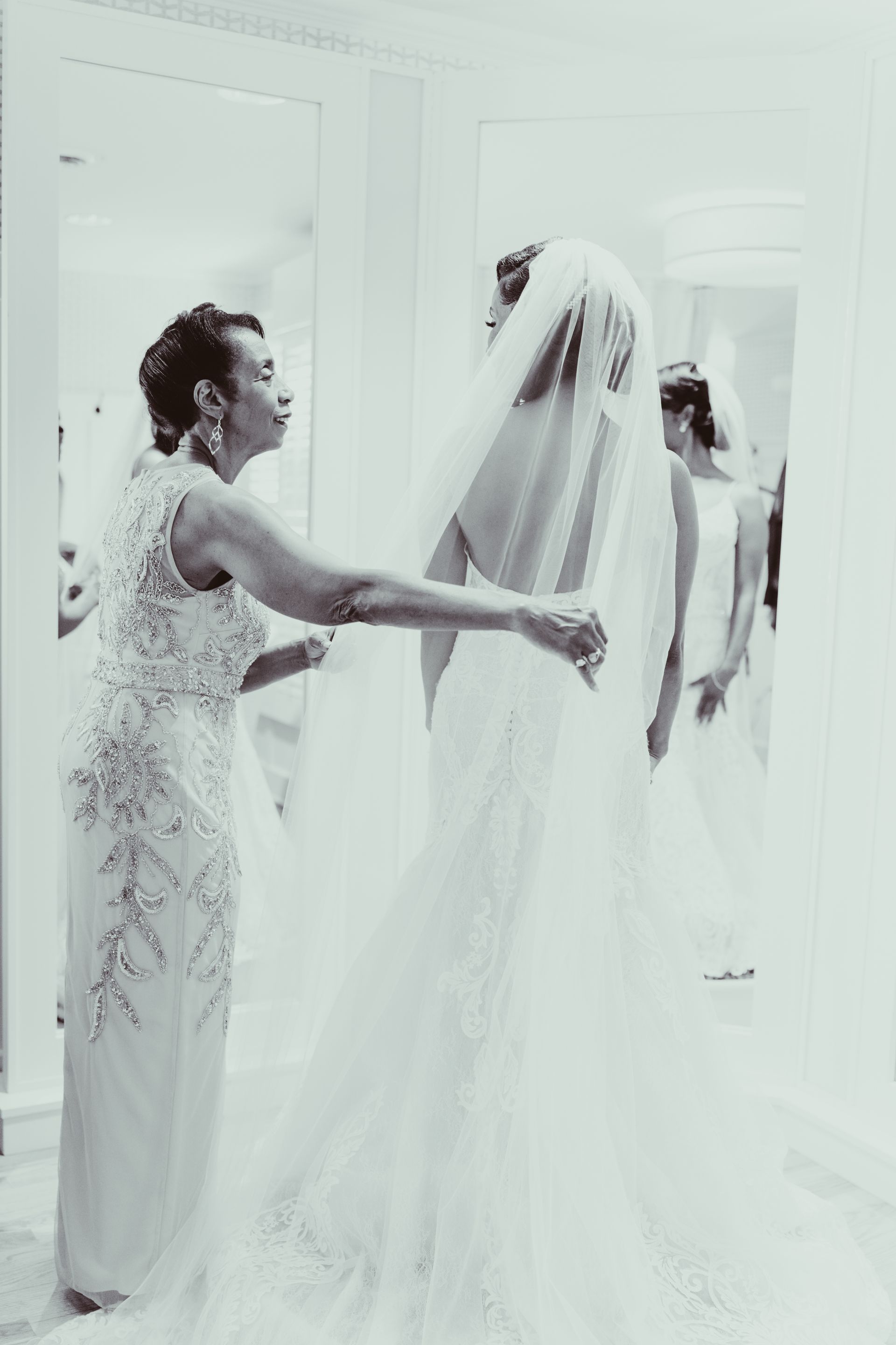 A woman is helping a bride get ready for her wedding in a black and white photo.