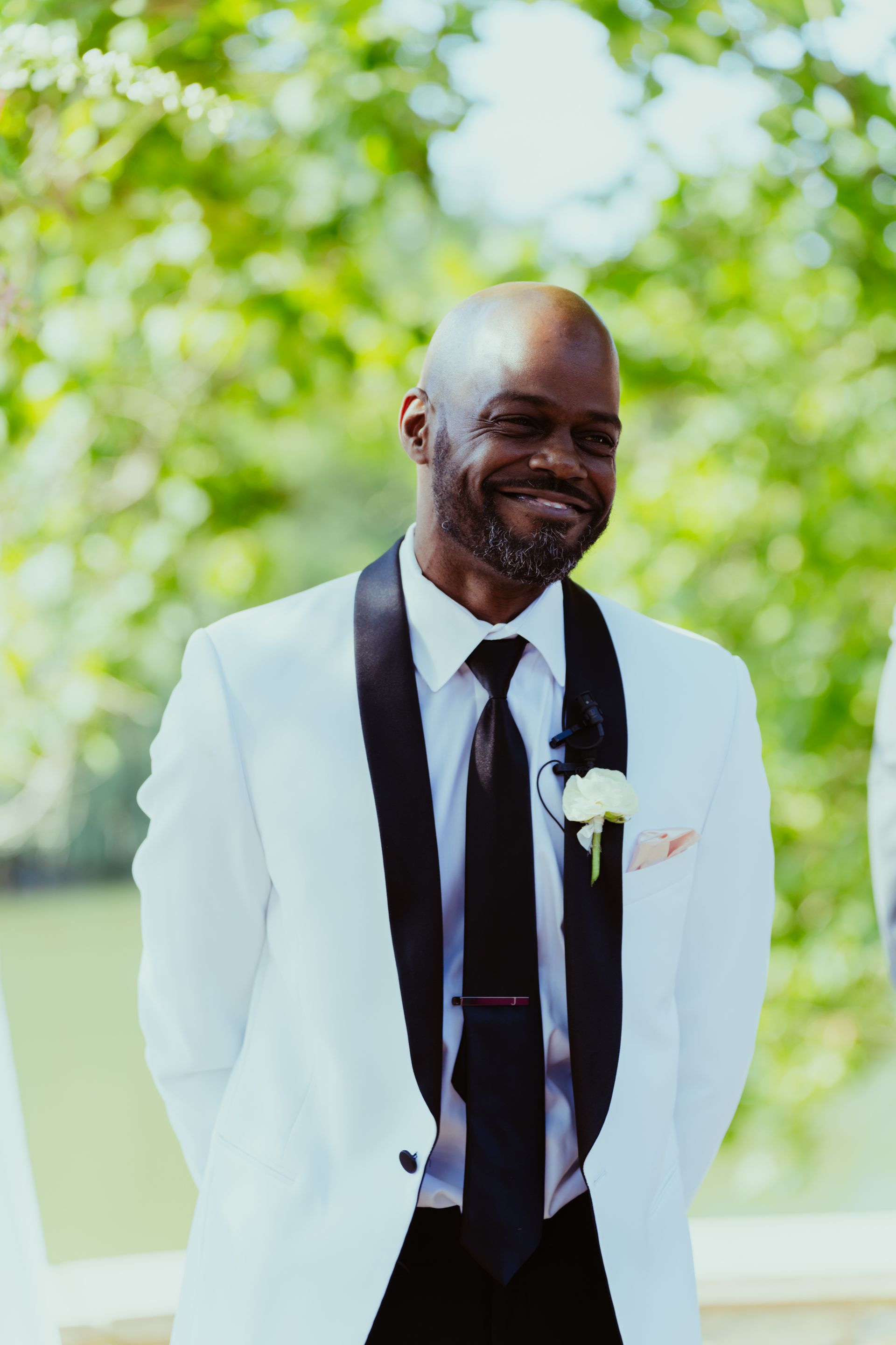 A man in a white suit and black tie is smiling