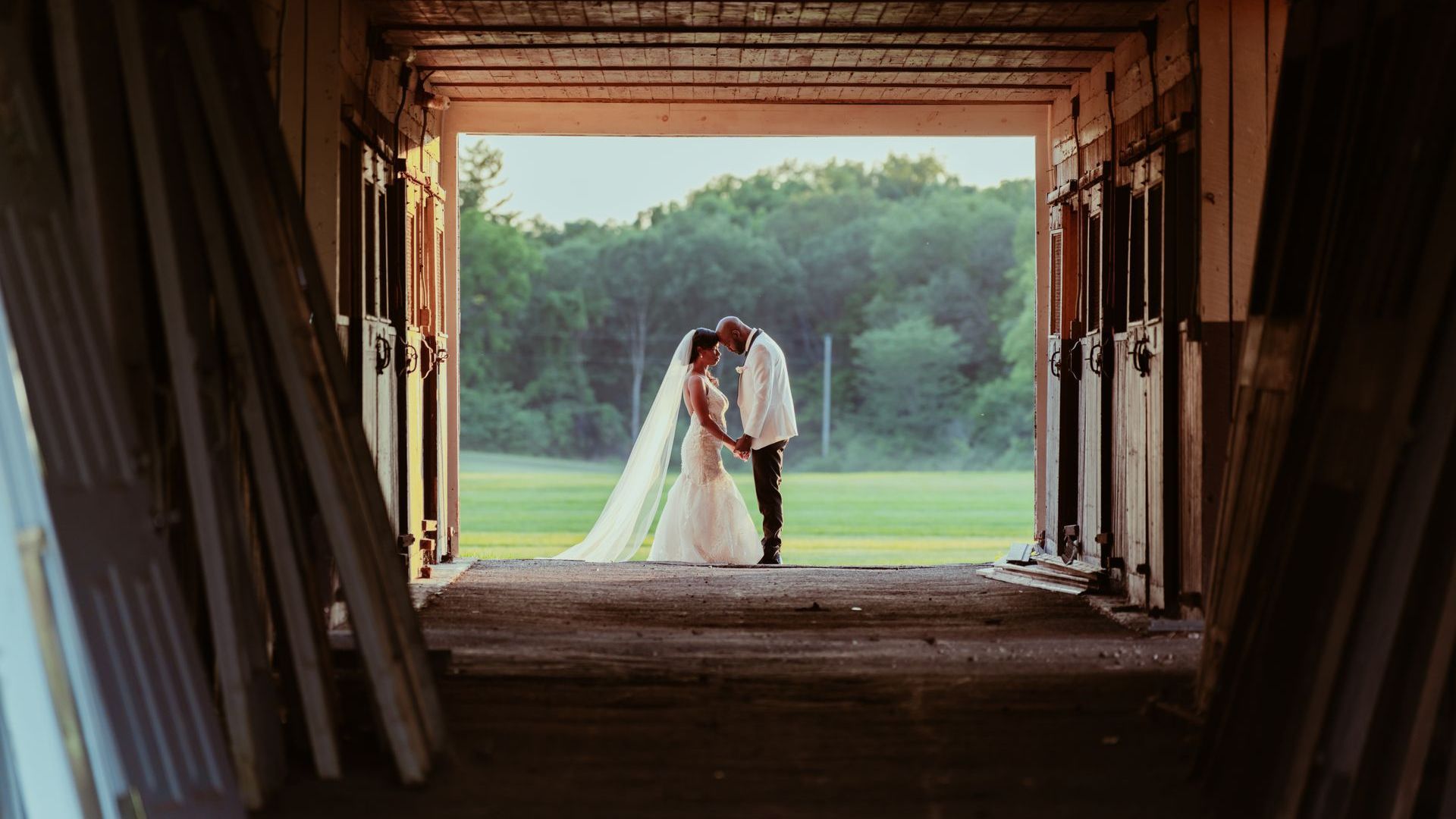 A bride and groom are kissing in a barn doorway.