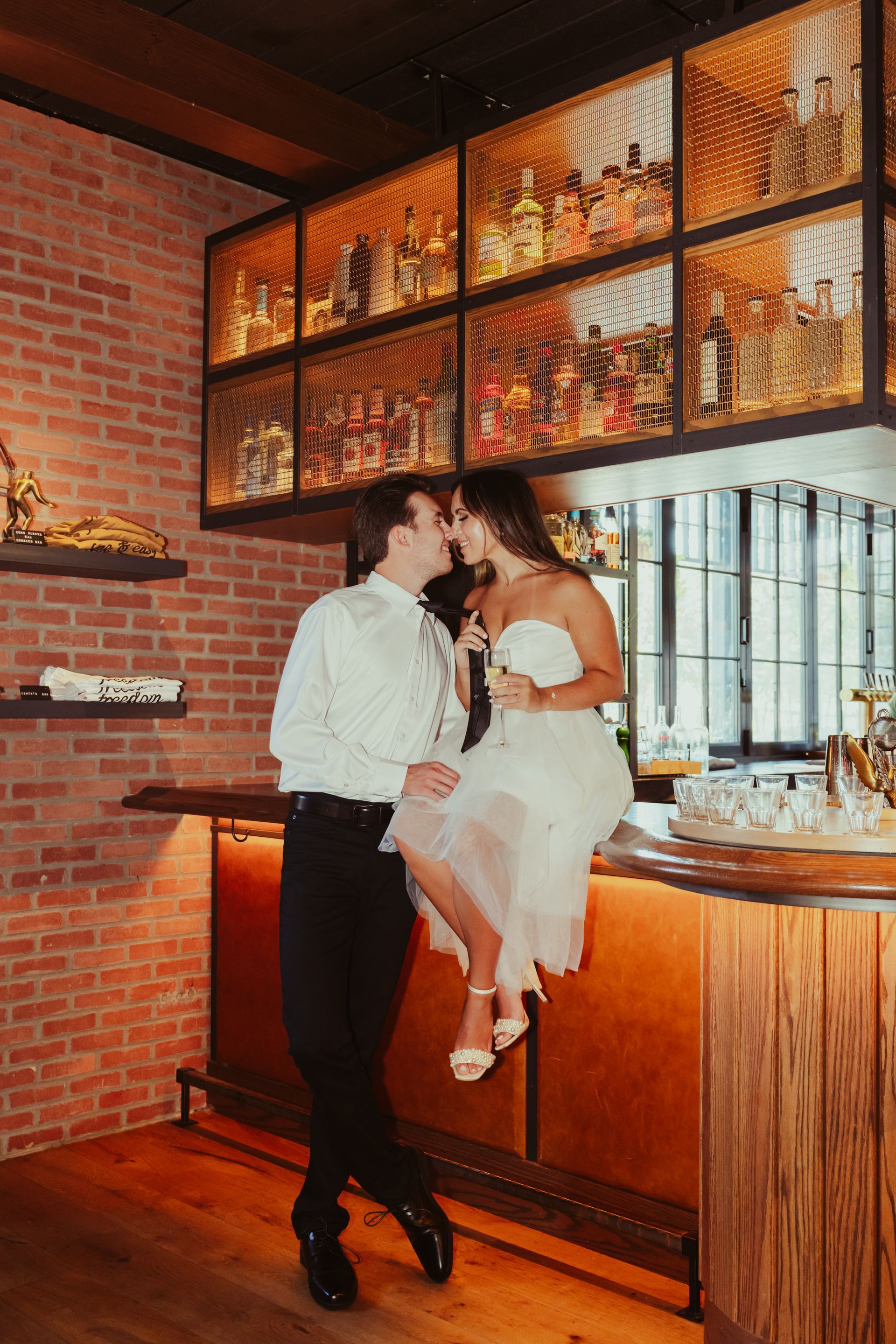 A bride and groom are kissing while sitting on a bar in a restaurant.