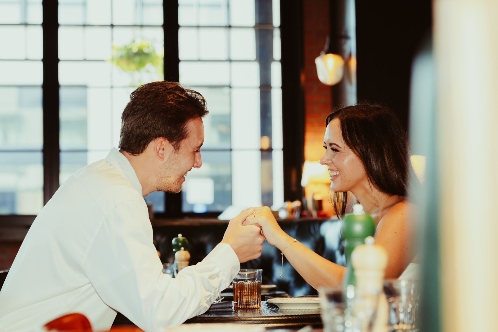 A man and a woman are holding hands while sitting at a table in a restaurant.