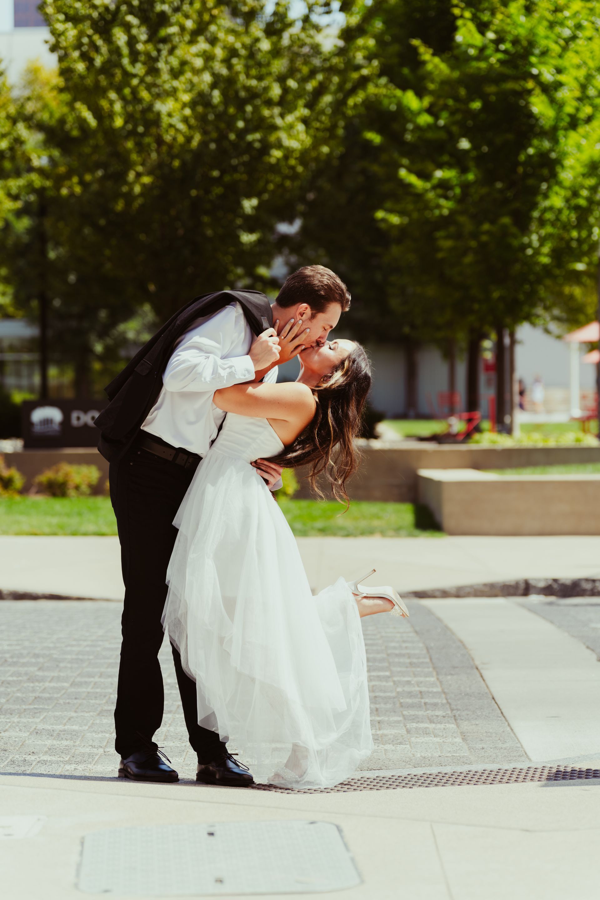 A bride and groom are kissing on the sidewalk.