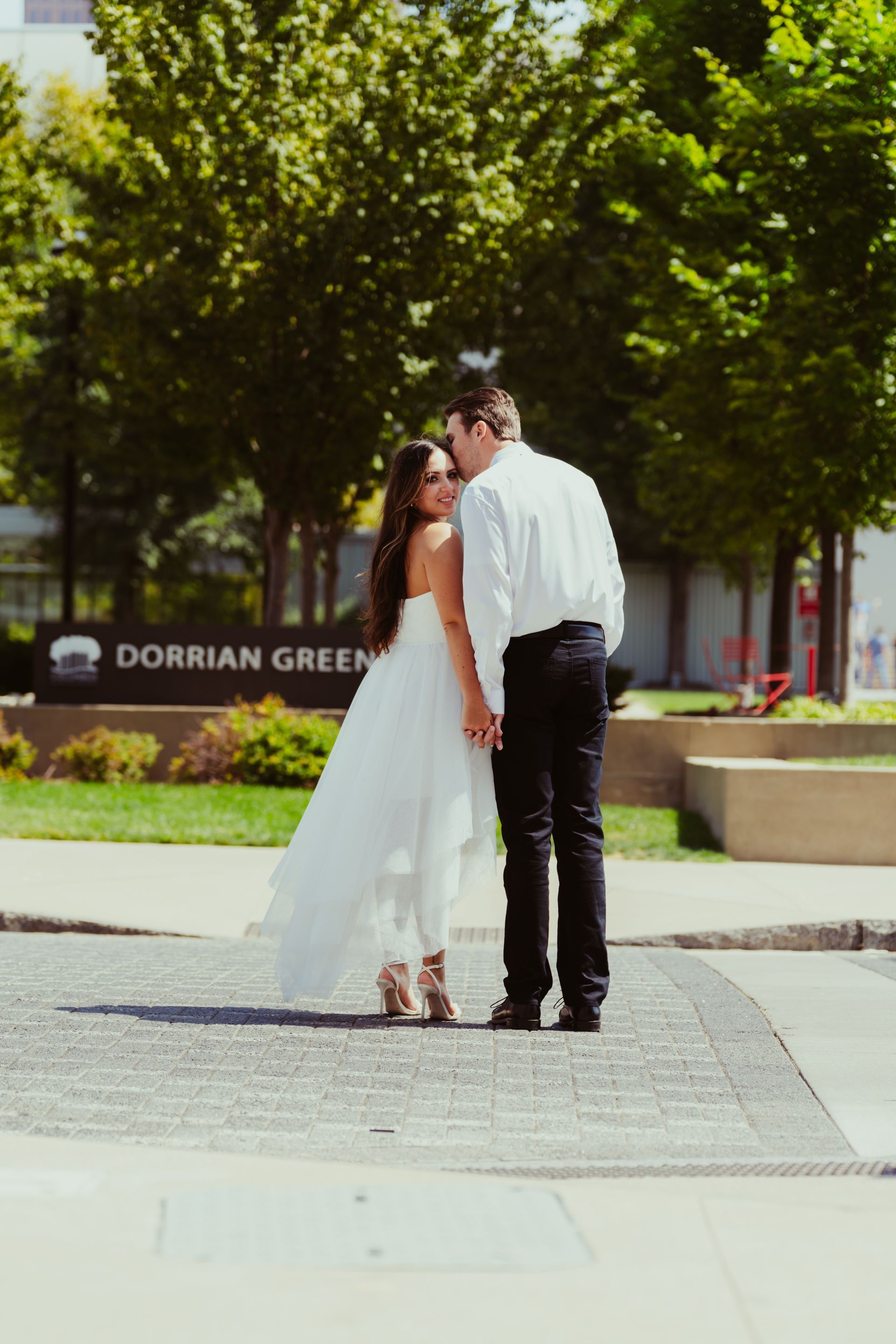 A bride and groom kissing on a sidewalk in front of a sign that says dorrian green.