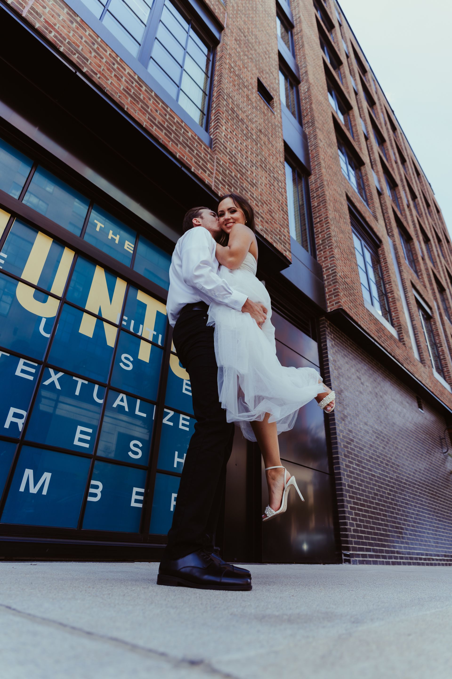 A bride and groom are kissing in front of a building.