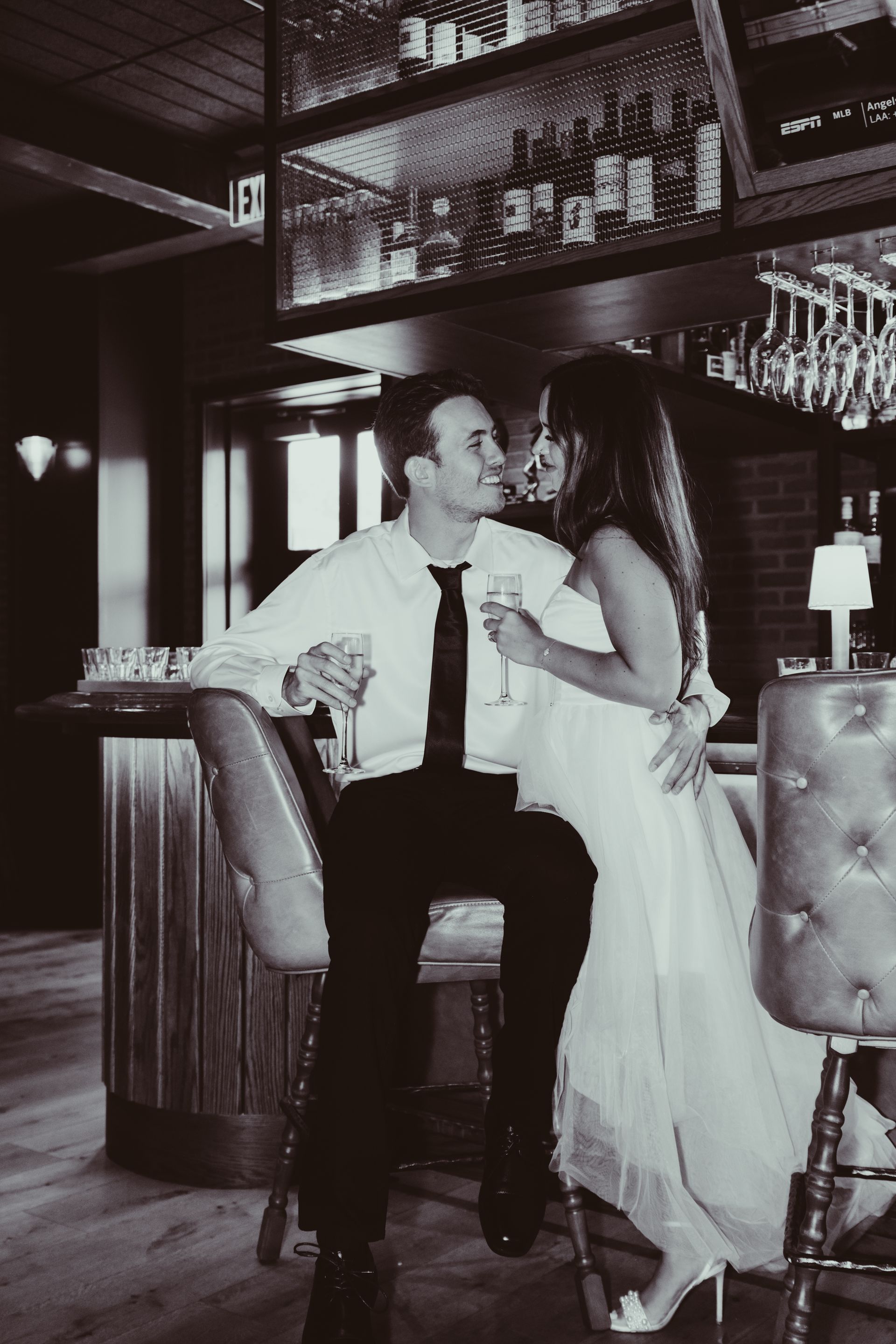 A black and white photo of a bride and groom sitting at a bar.