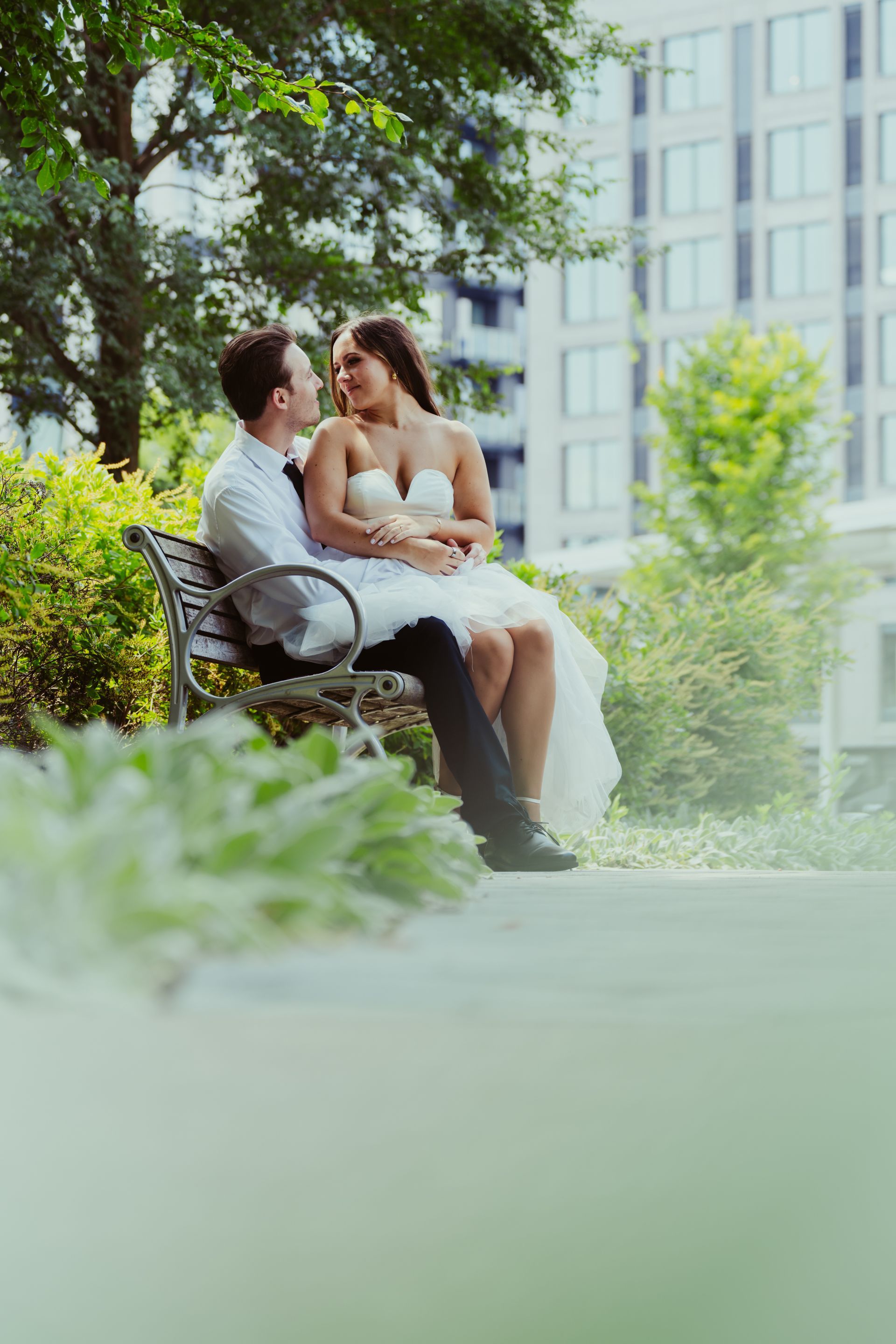 A bride and groom are sitting on a park bench.