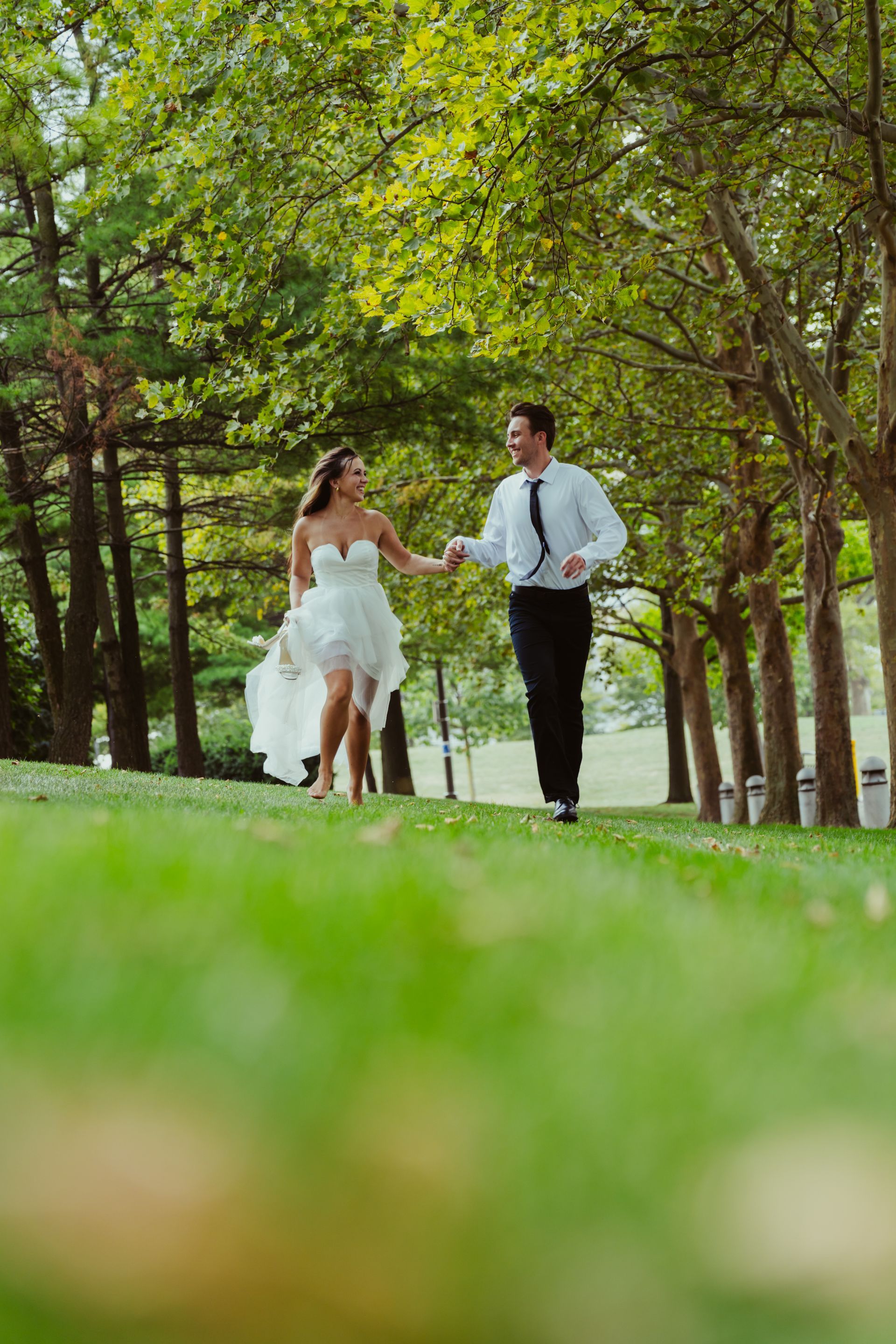 A bride and groom are holding hands while walking through a park.