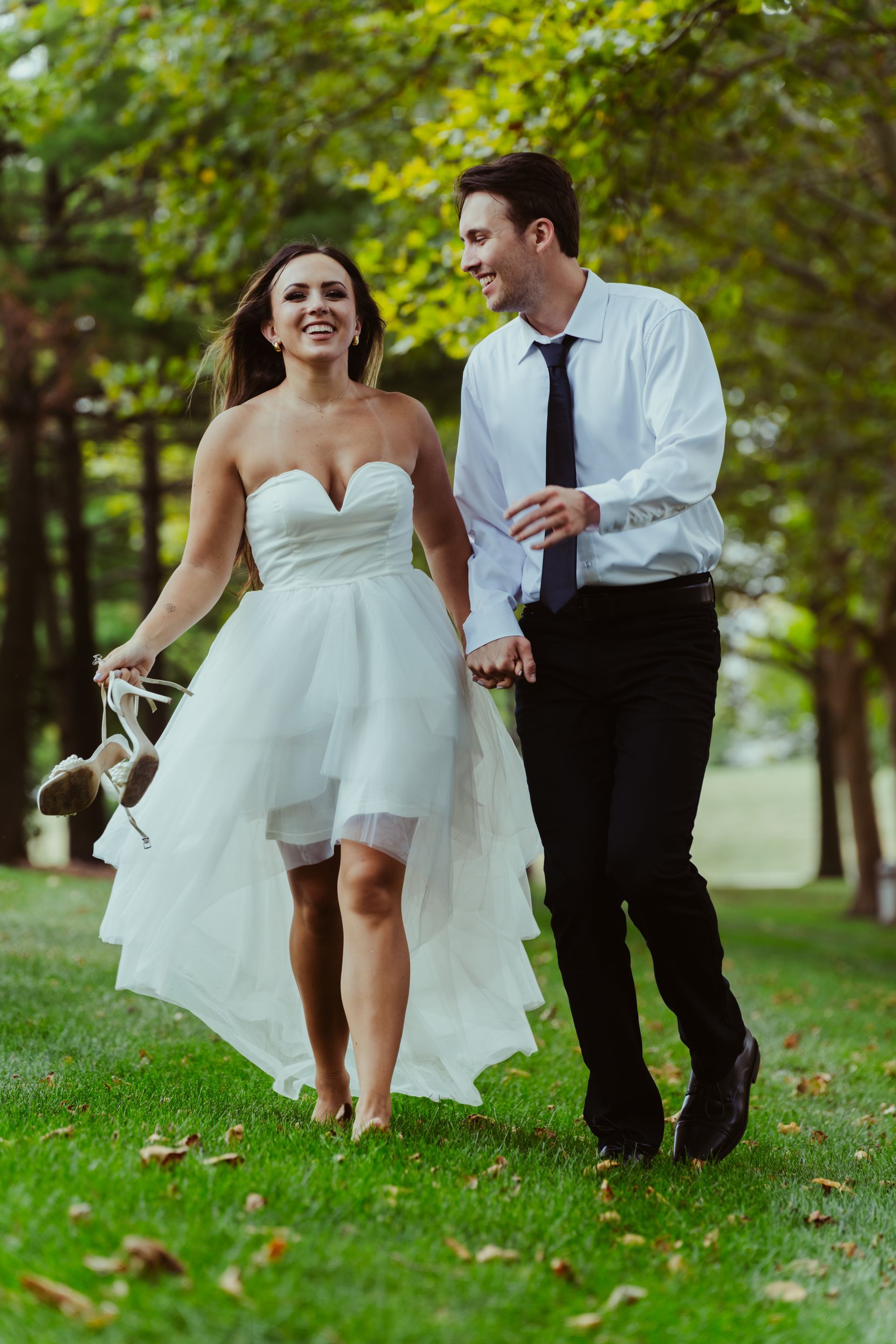 A bride and groom are walking through a park holding hands.