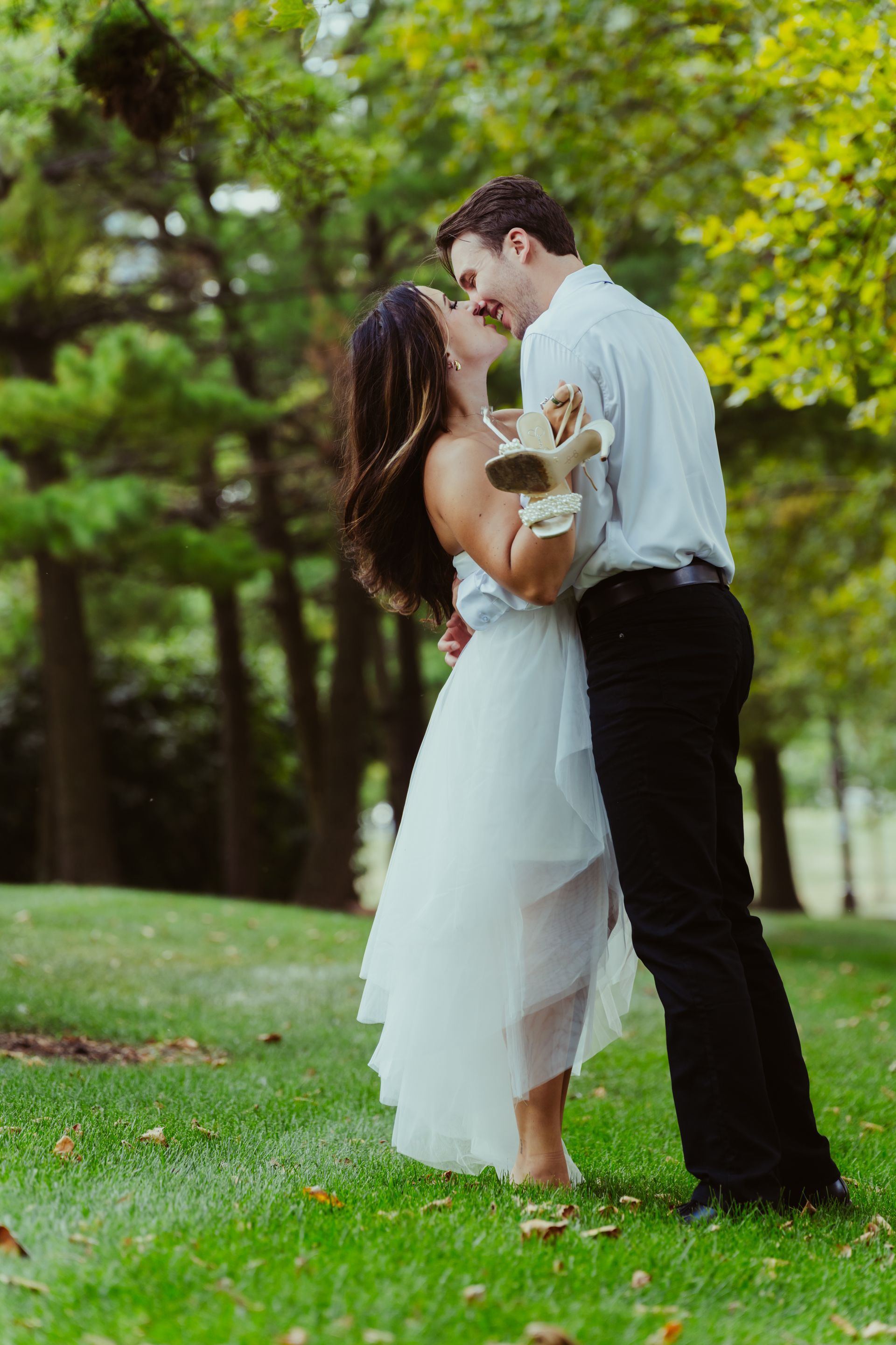 A bride and groom are kissing in the grass in a park.