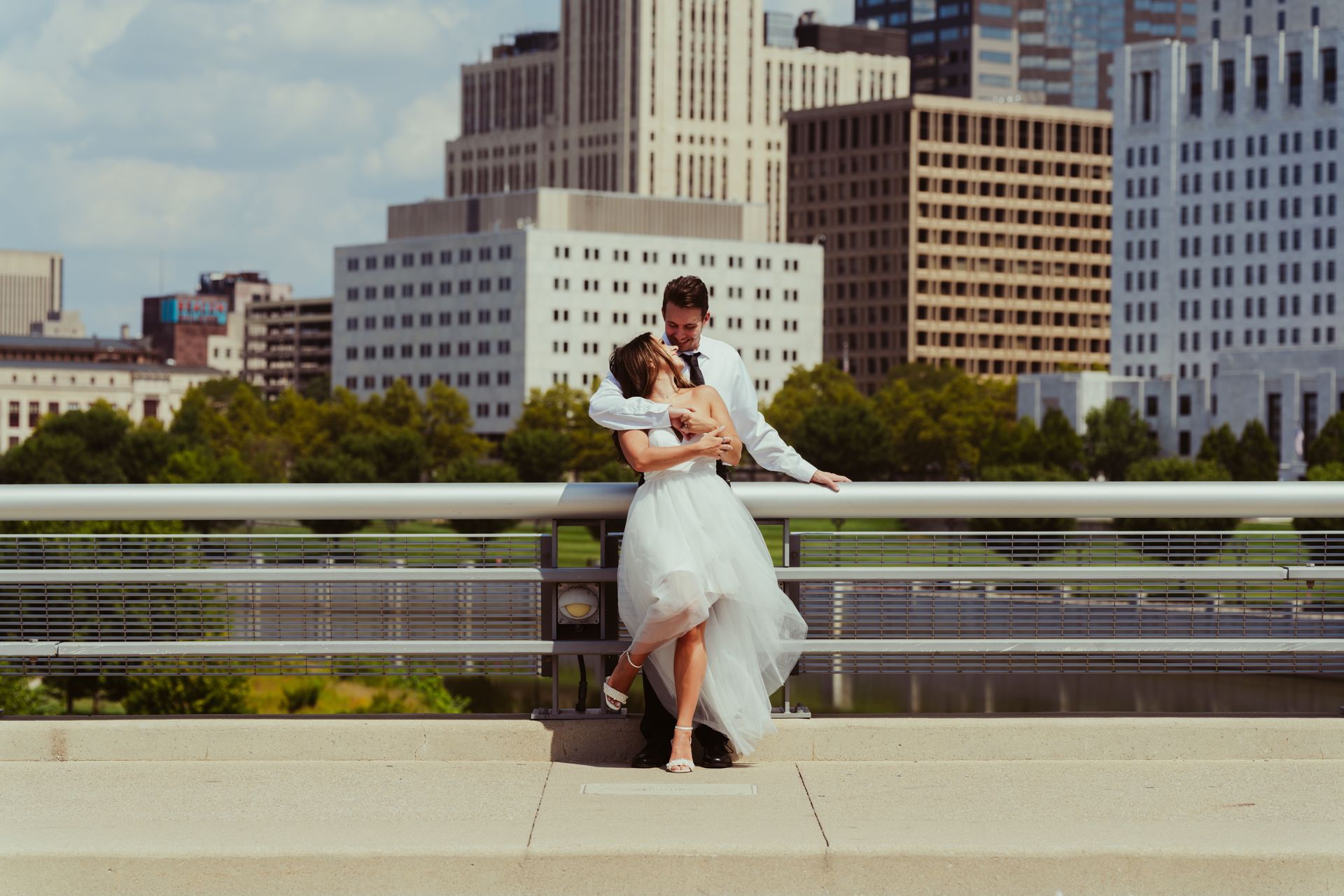 A bride and groom are hugging on a bridge in front of a city skyline.