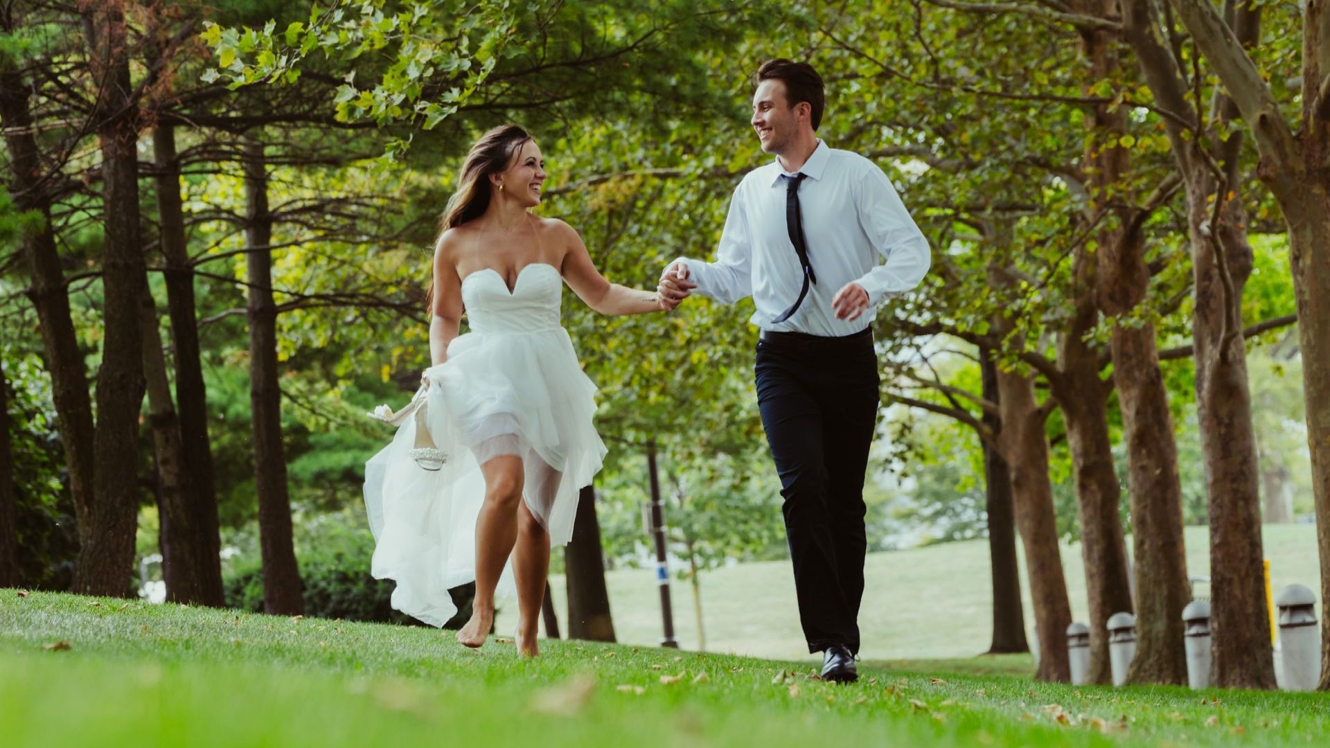 A bride and groom are walking through a park holding hands.