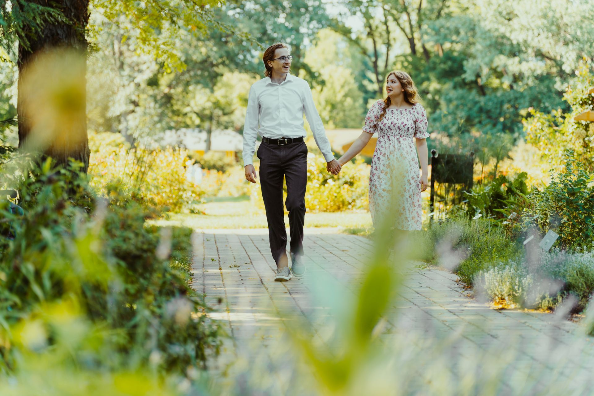 A man and a woman are walking down a path in a park holding hands.