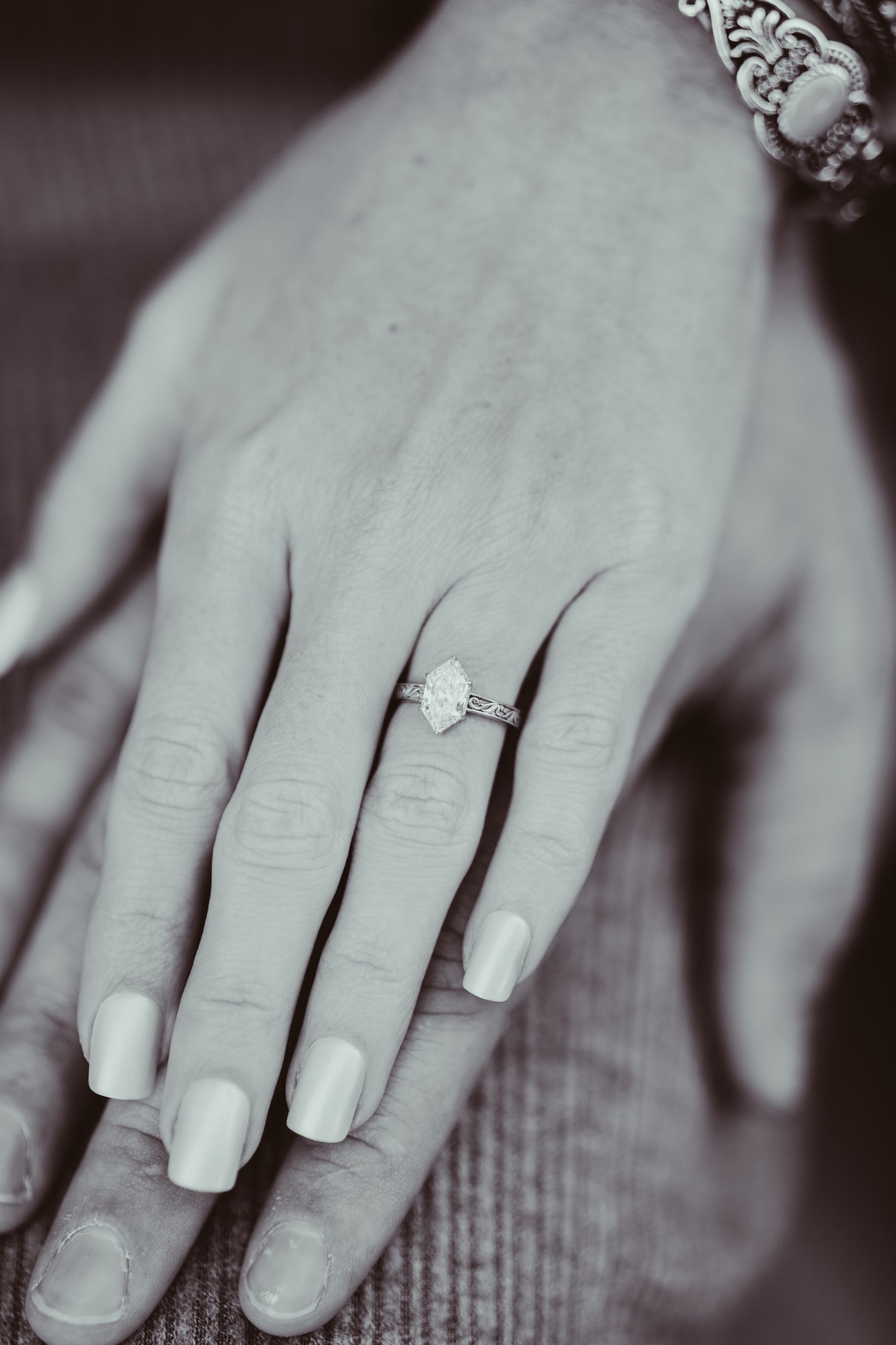 Hand with engagement ring resting on another hand. Black and white photo.
