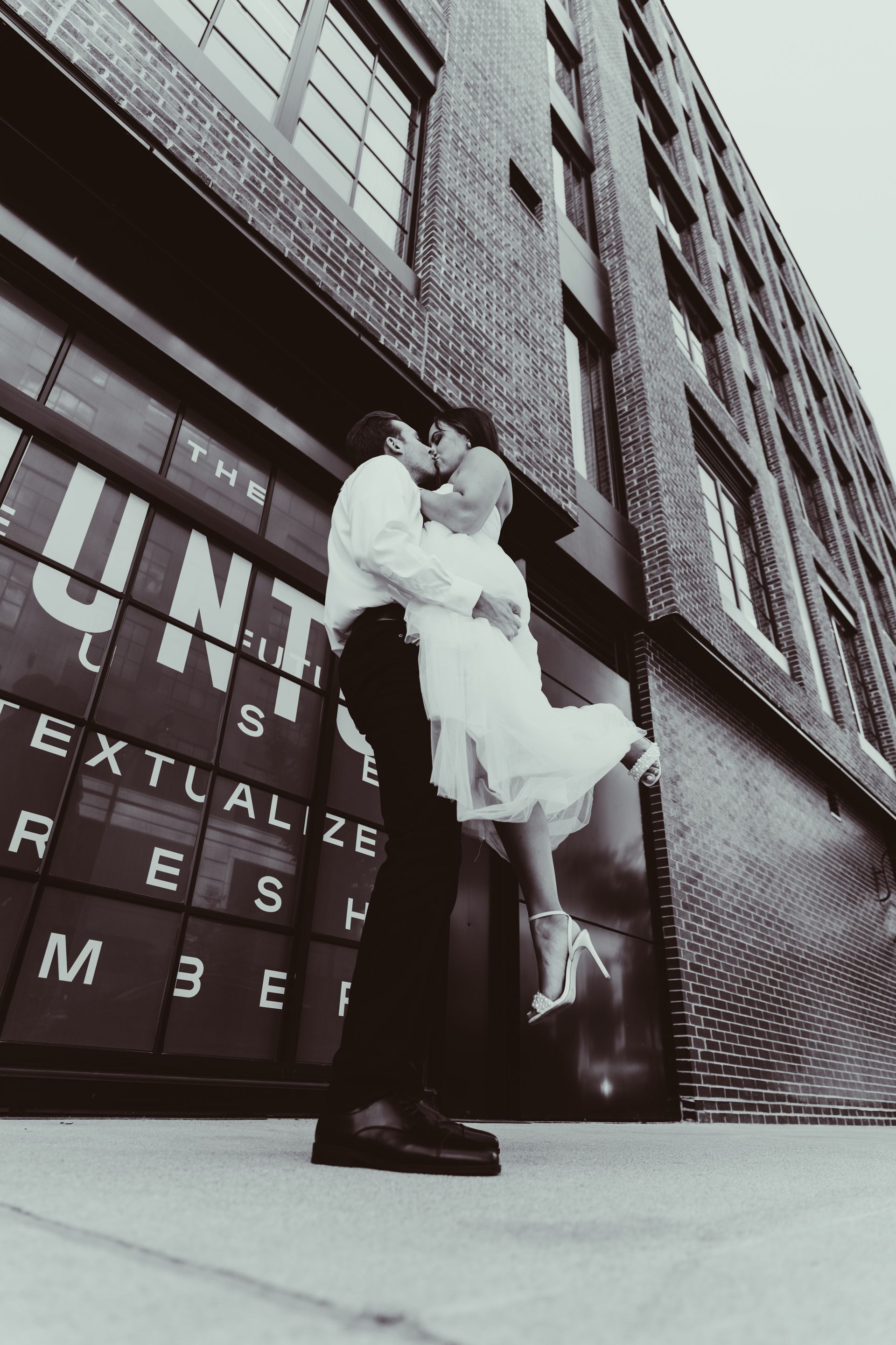 A man is holding a woman in his arms in front of a building that says the unit