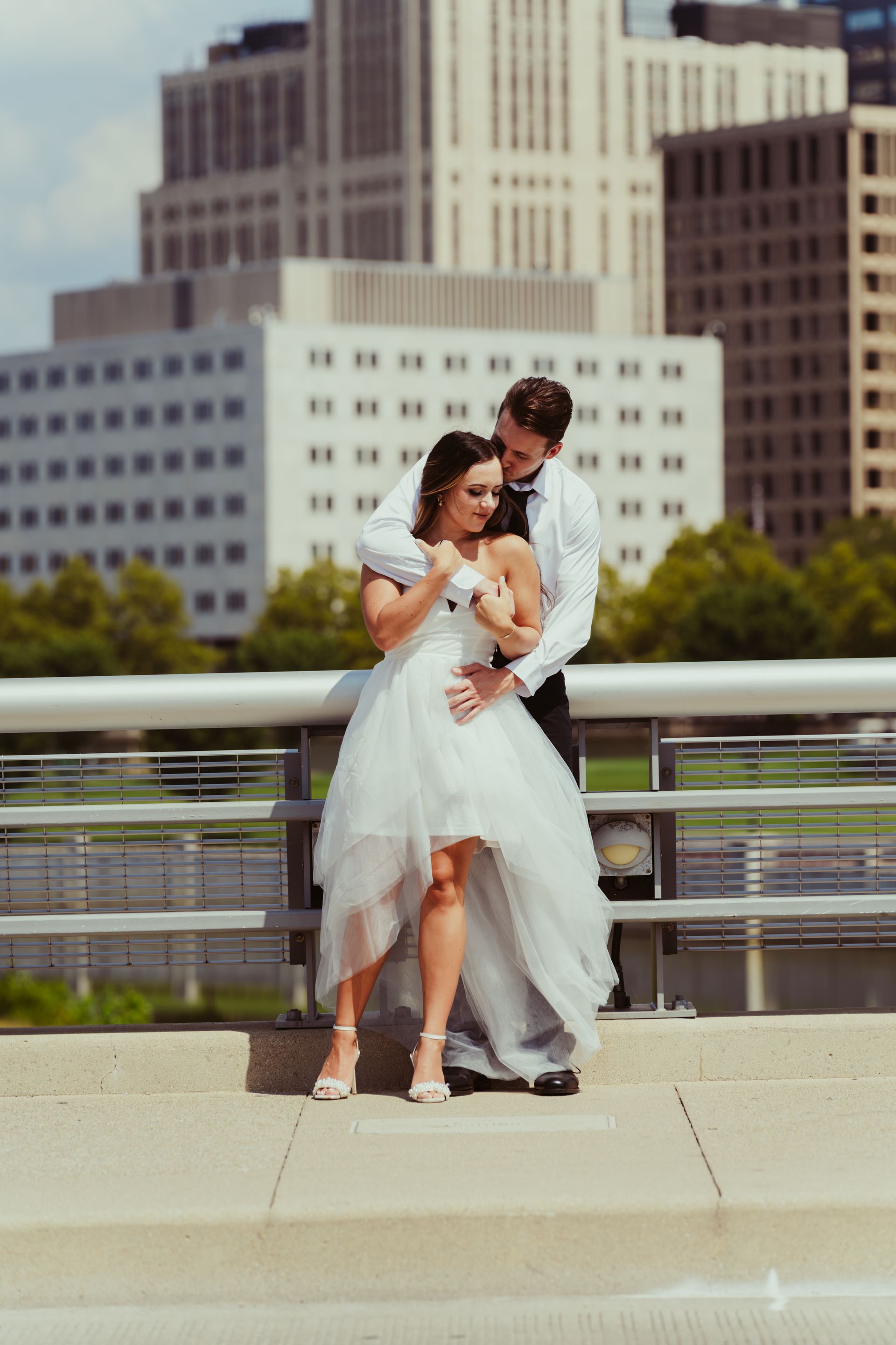 A bride and groom are posing for a picture on a bridge in front of a city skyline.