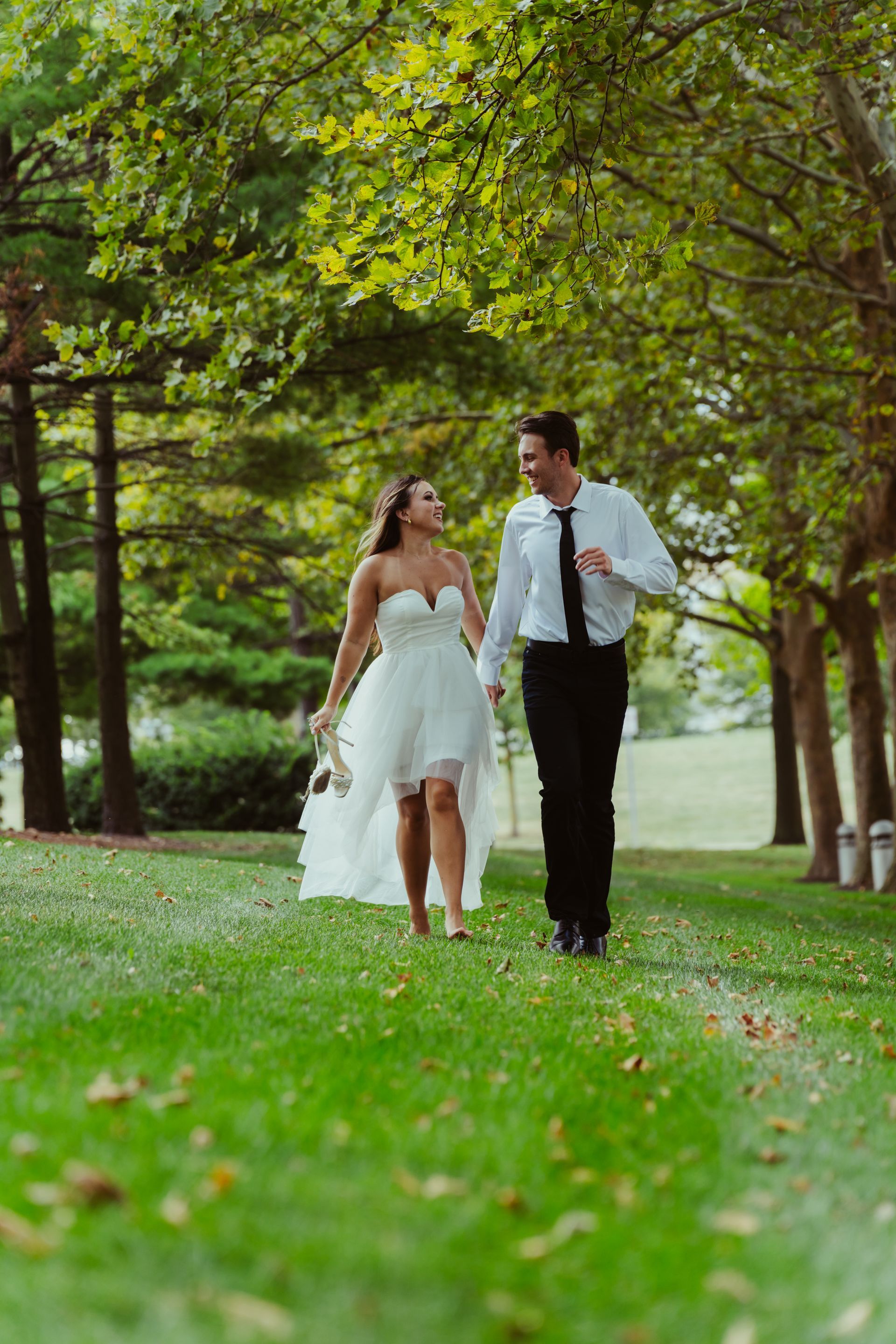 A bride and groom are walking through a park holding hands.