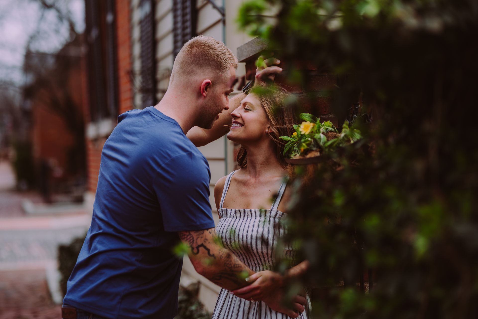 A close-up shot of a hand wearing a ring resting on an arm with tattoos, with a smiling person blurred in the background.