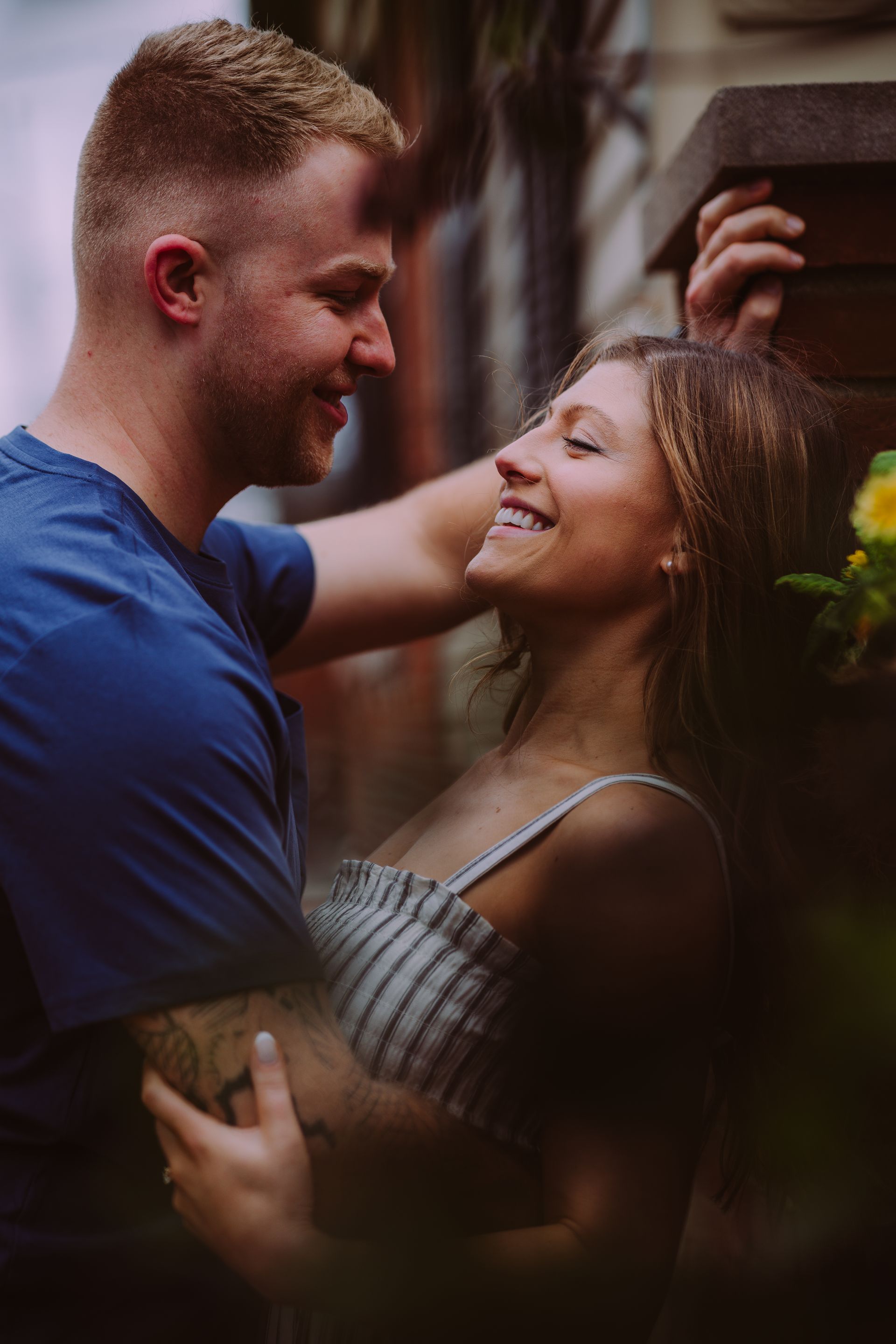 A couple in casual clothing smiles at each other in a close embrace outdoors.