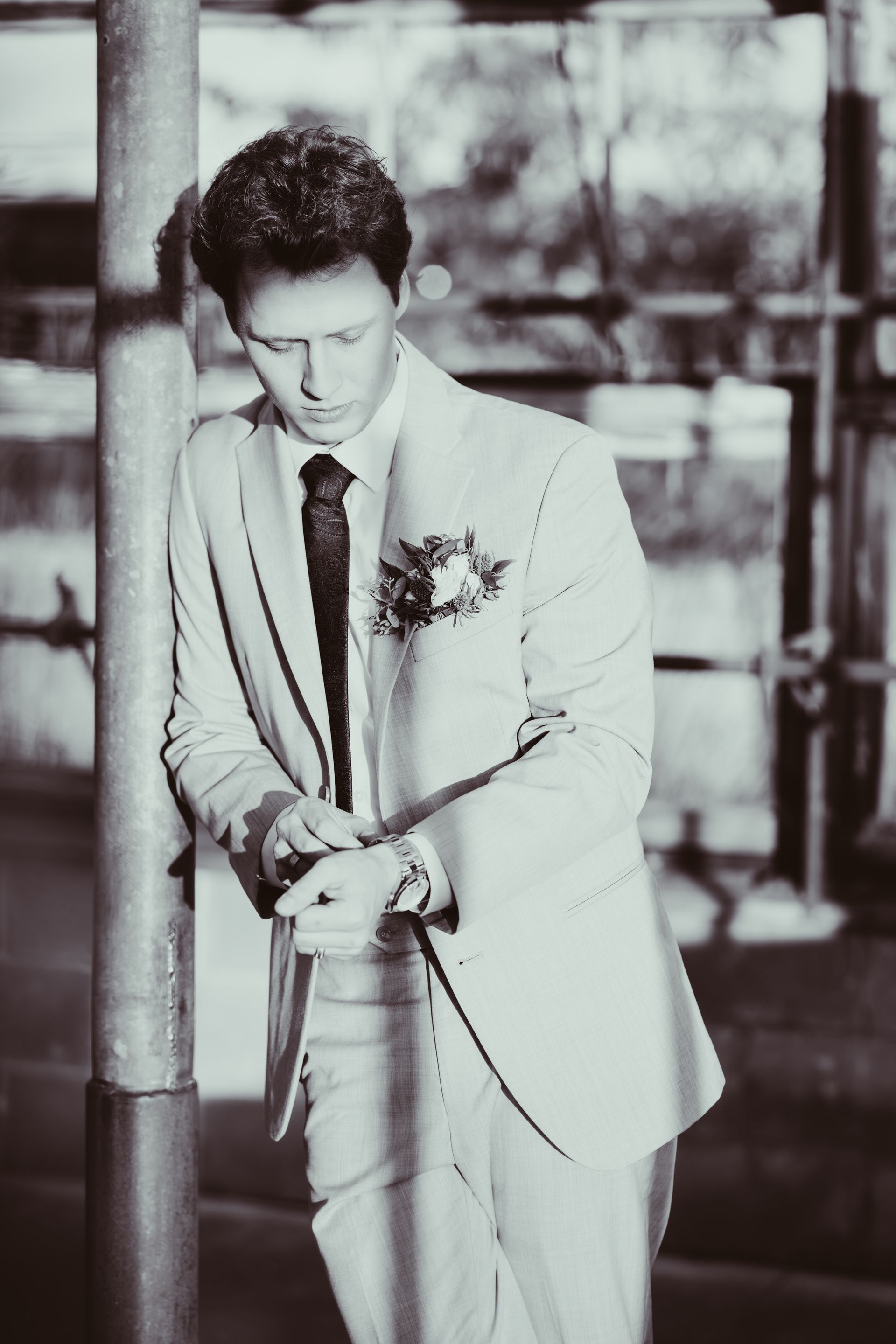 Man in suit adjusts cuff, leans against a pole.