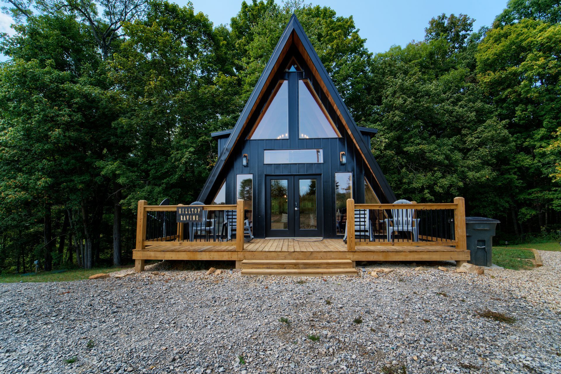 A small a frame cabin with a large deck in the middle of a forest.