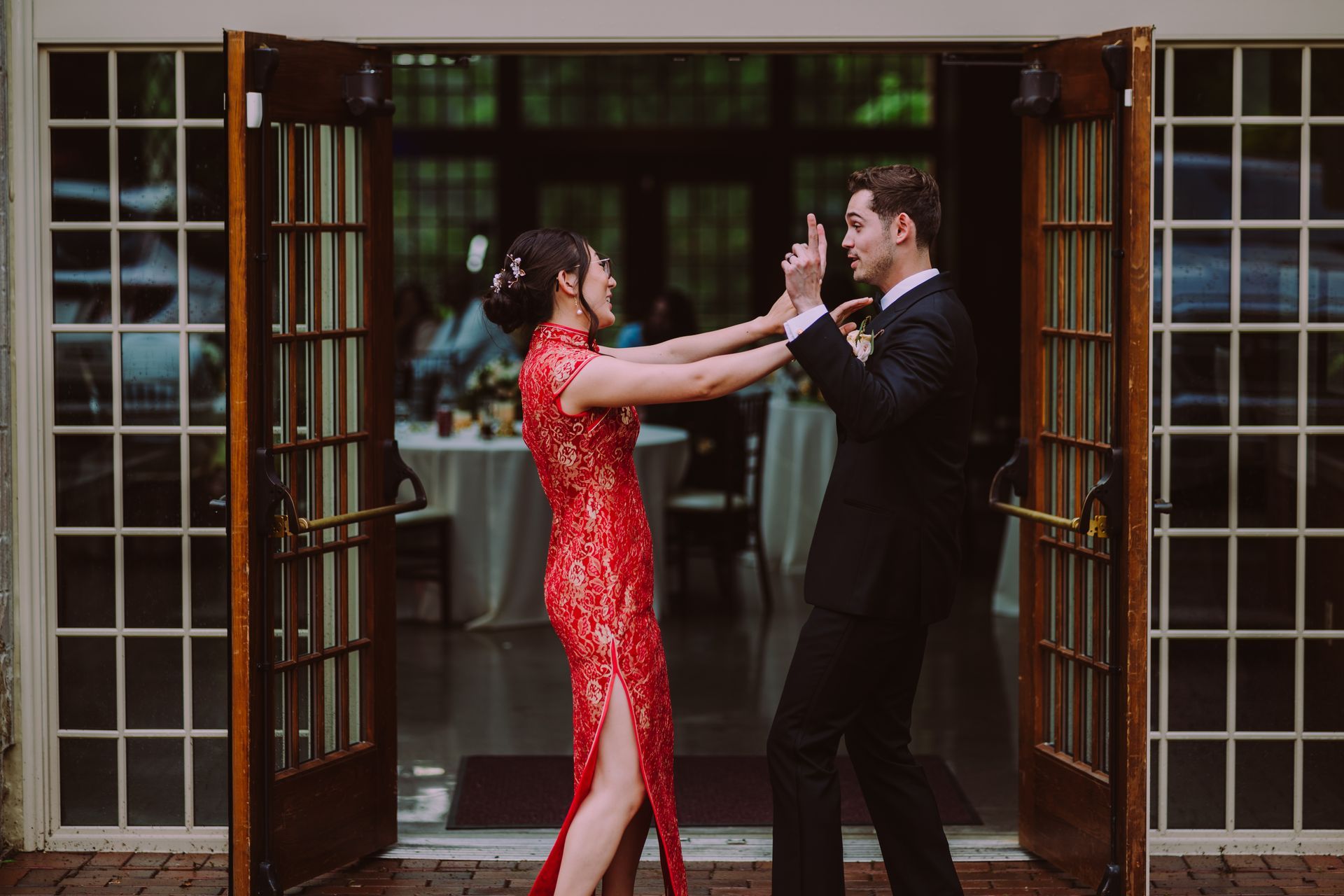 Couple dancing in a doorway, woman in red dress and man in black suit, hands raised.