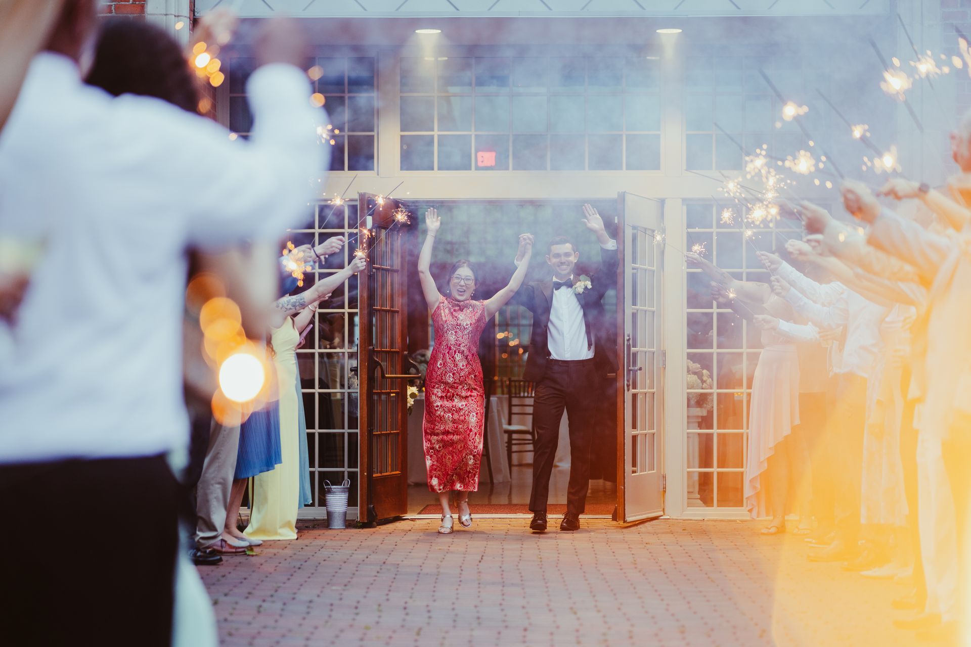 Wedding couple exiting a building with raised arms as guests cheer nearby
