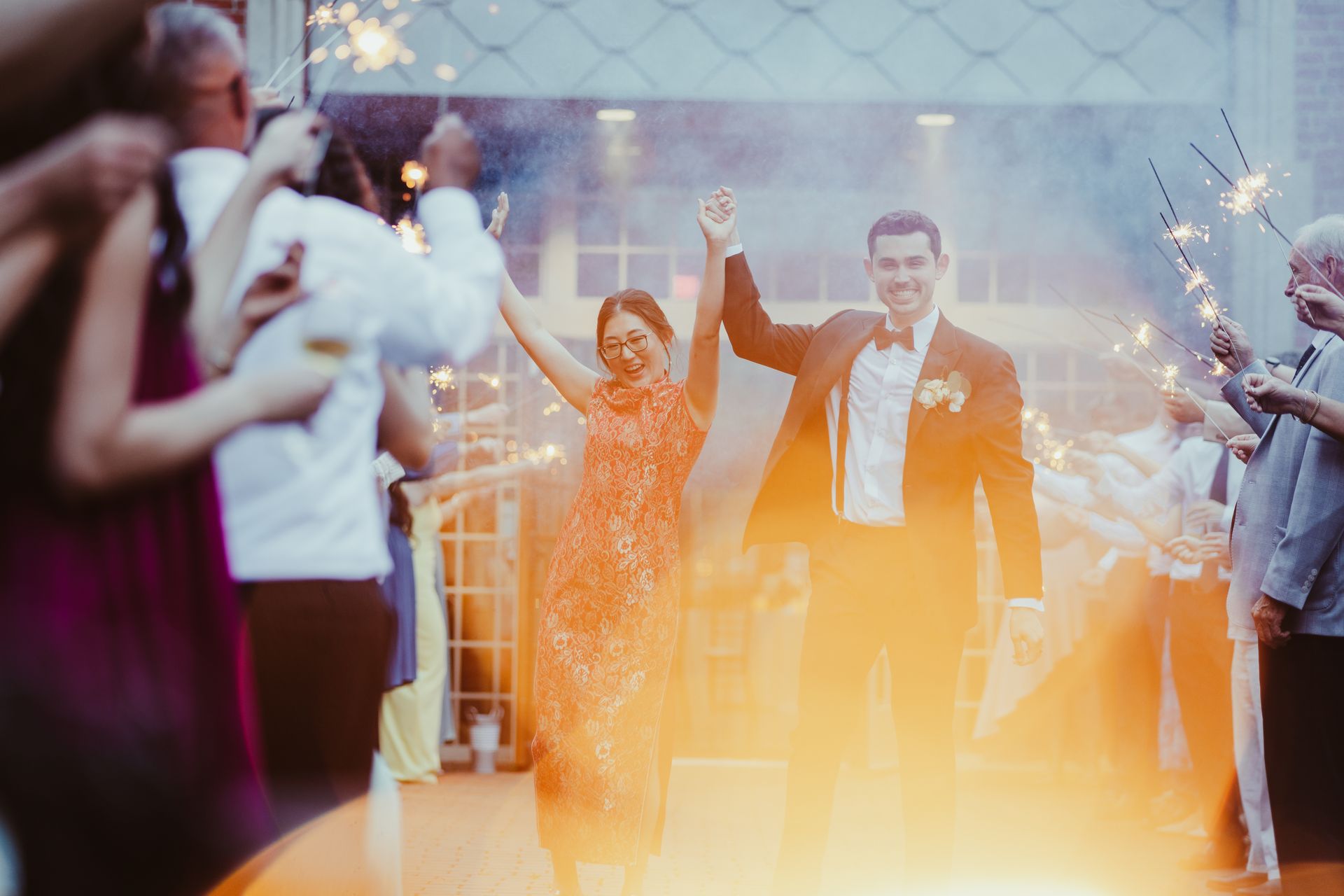 Wedding couple cheering as guests hold sparklers at an outdoor celebration