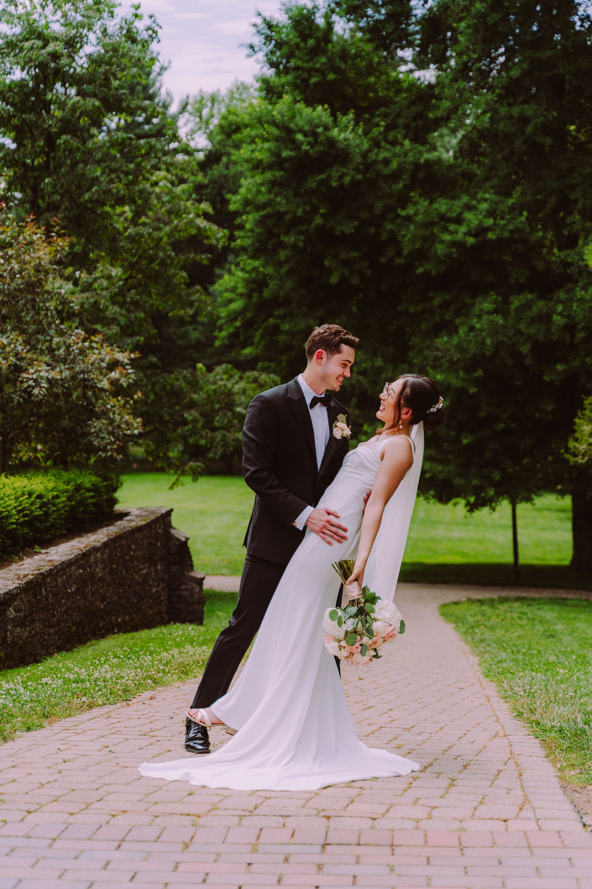 Bride and groom posing on a garden path, the groom dipping the bride in her white dress.