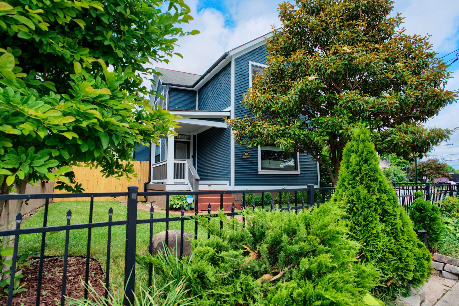 A blue house with a black fence and trees in front of it.