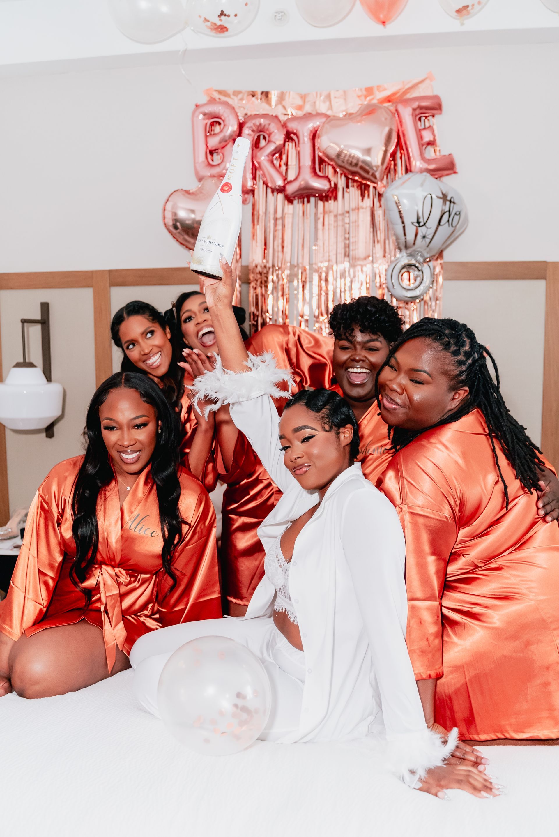 A bride and her bridesmaids are posing for a picture on a bed.