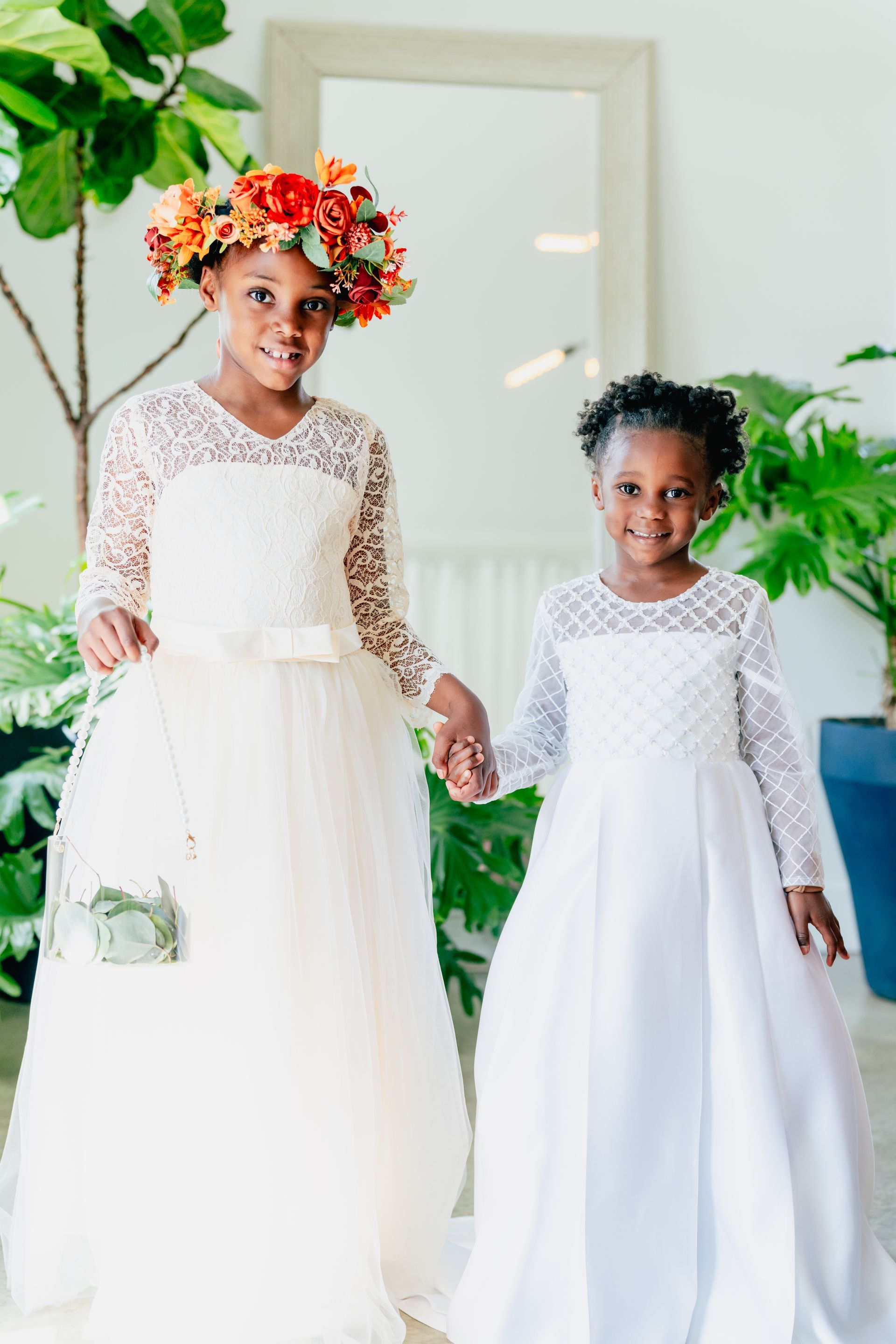 Two flower girls are holding hands and wearing white dresses.