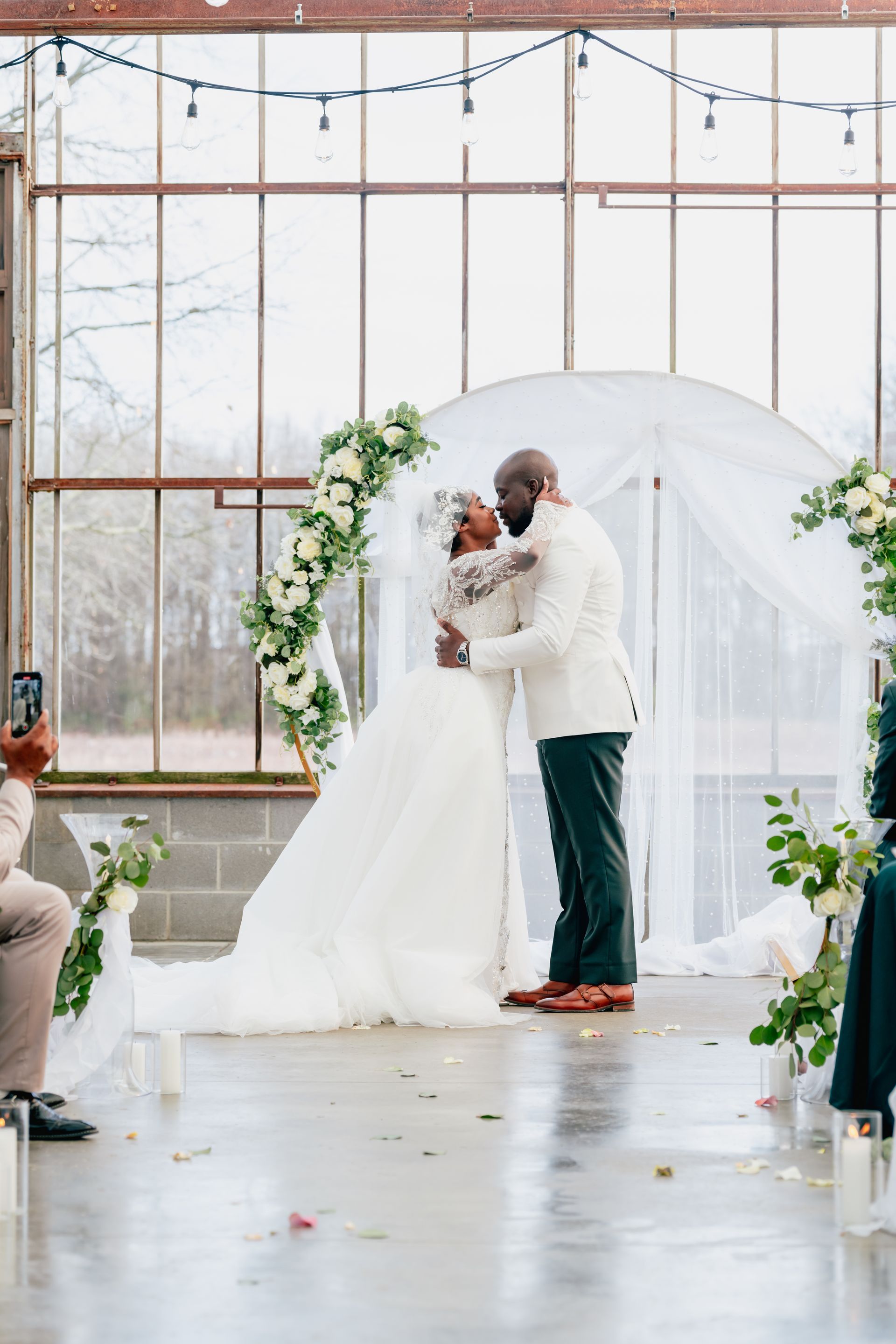 A bride and groom are kissing during their wedding ceremony in jorgensen farm oak grove greenhouse.
