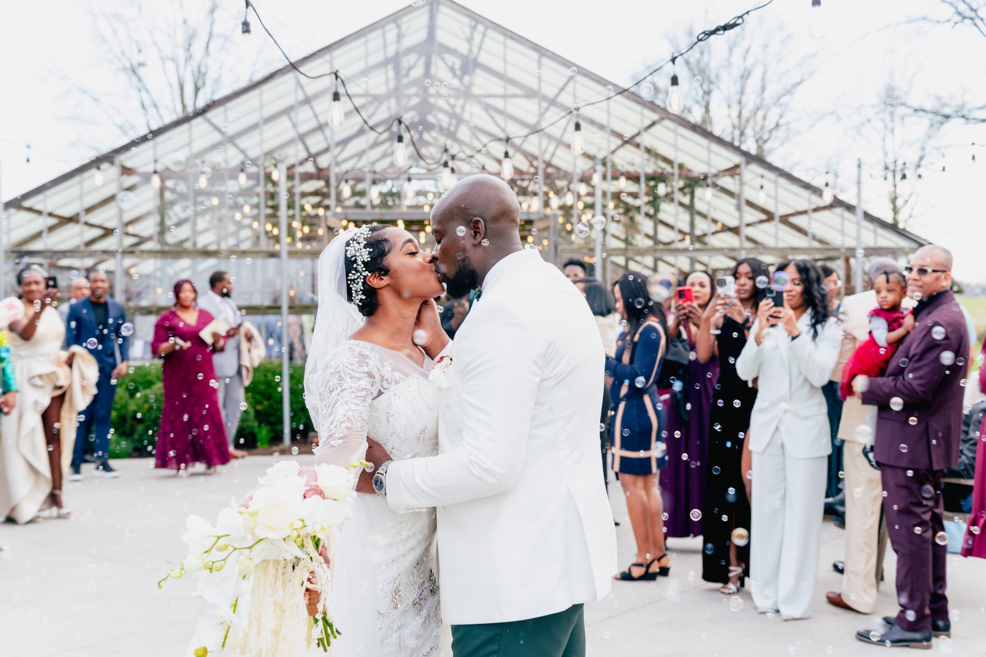 A bride and groom kissing in front of a jorgensen farms oak grove greenhouse.