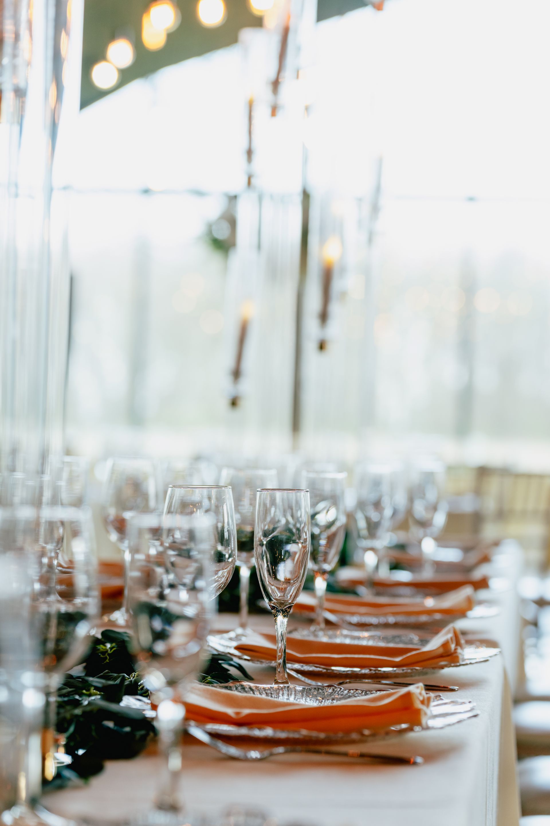A long table with plates , glasses , napkins and candles on it.