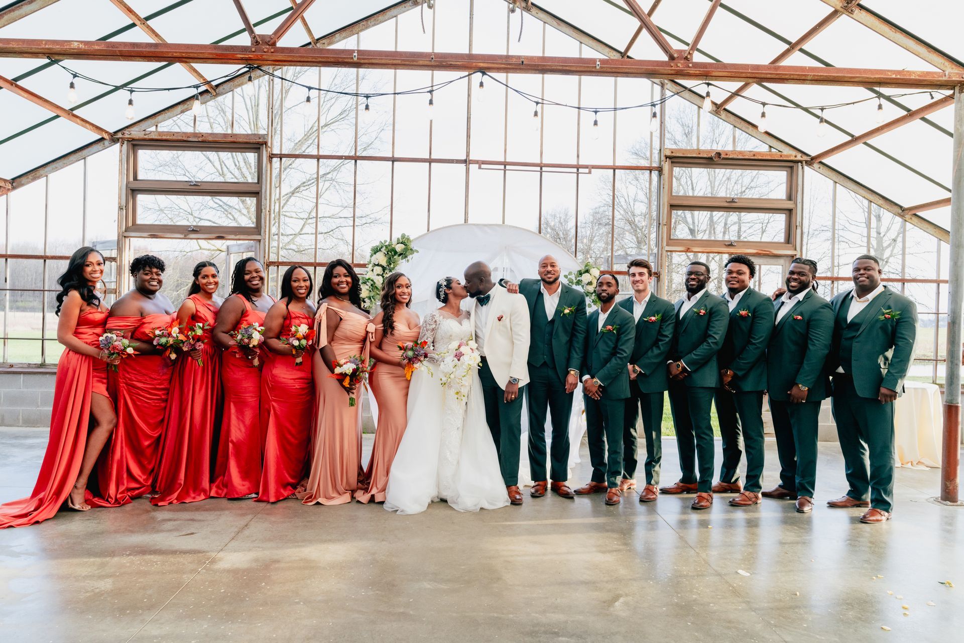 A bride and groom are posing for a picture with their wedding party in a jorgensen farms oak grove greenhouse.