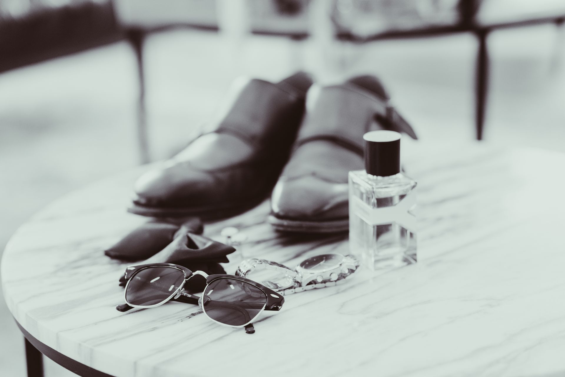 A pair of shoes , sunglasses , and a bottle of perfume are on a table.
