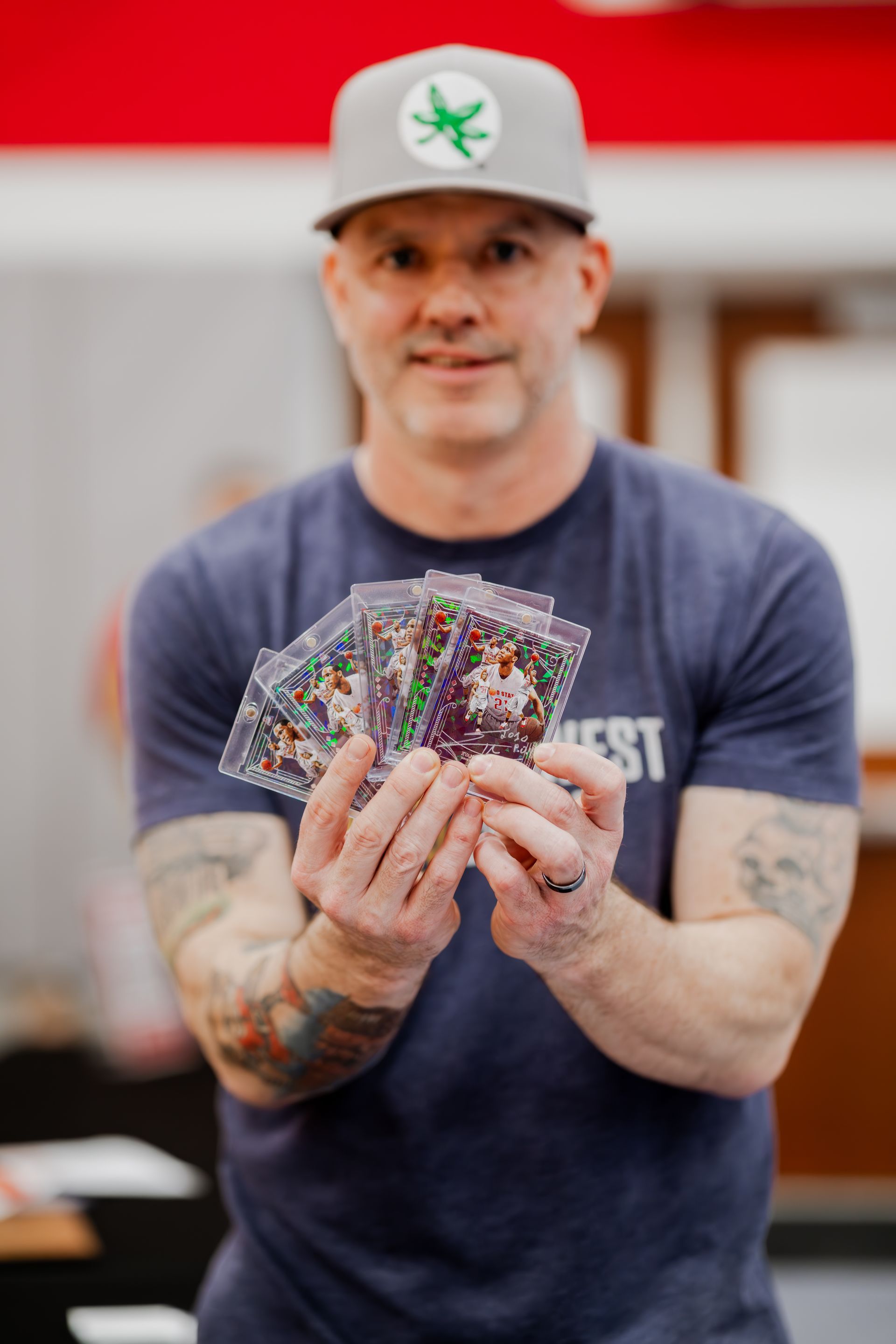 Man holding cards, smiling, wearing hat and dark blue shirt with 