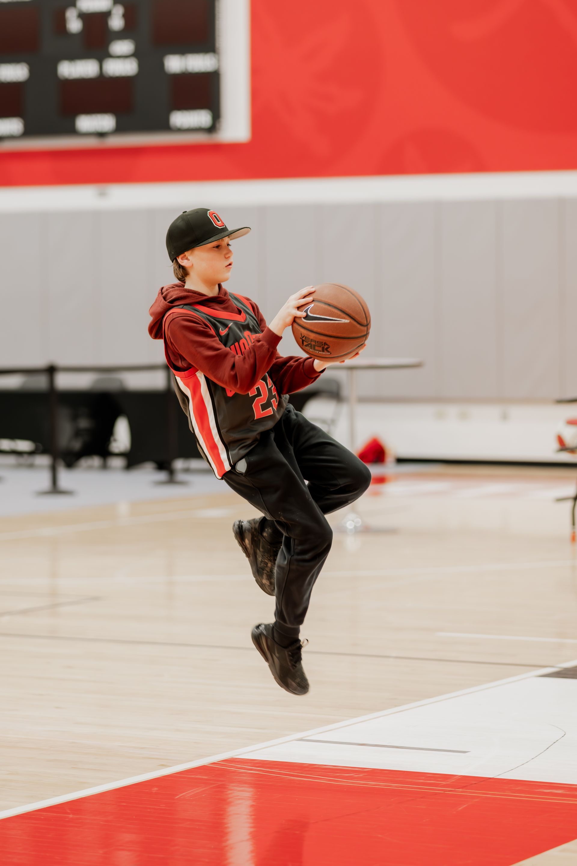 Person in a basketball uniform jumps, holding the ball, in a gymnasium.Midwest Cards | Event Photography