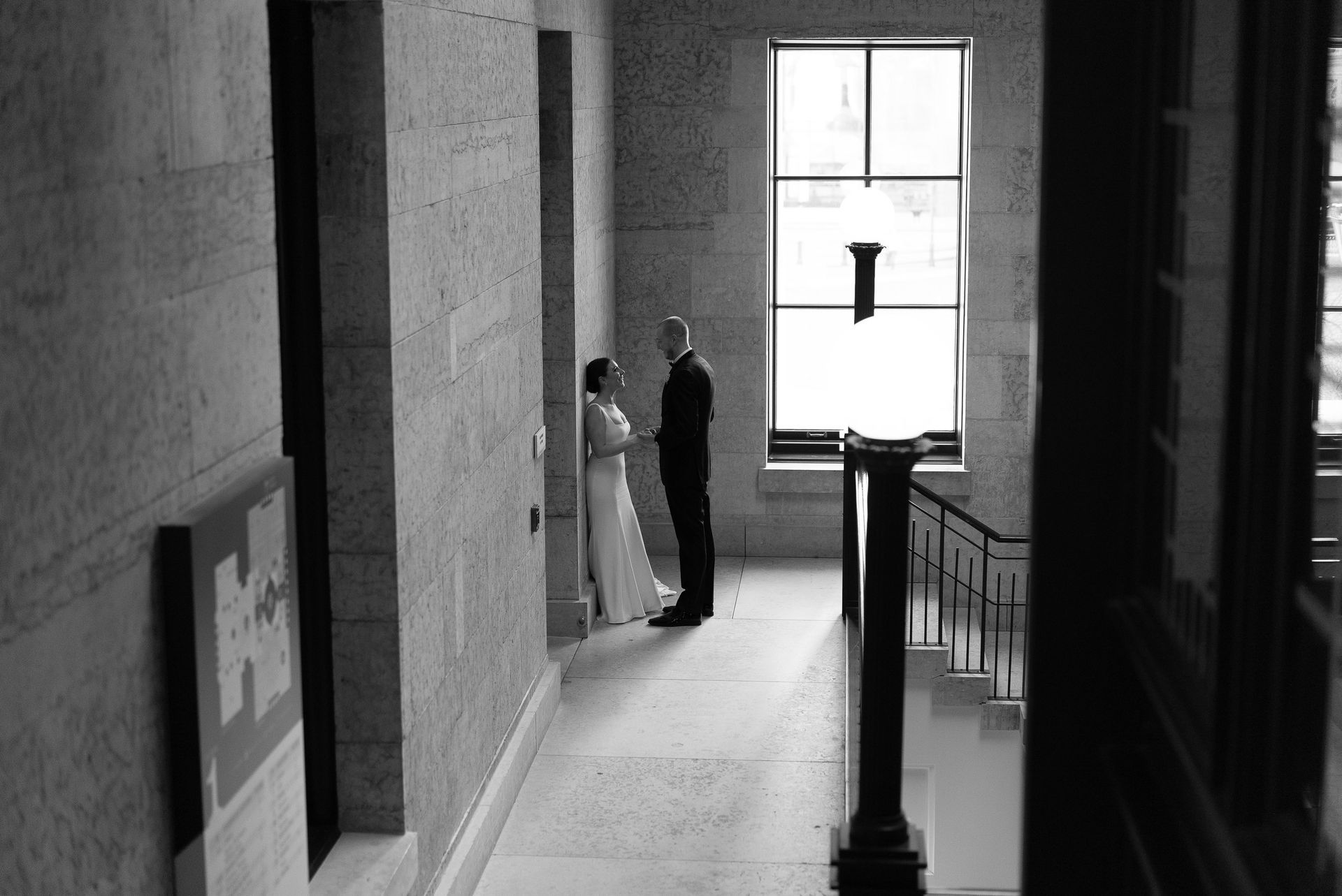 a black and white photo of a bride and groom standing in a hallway .