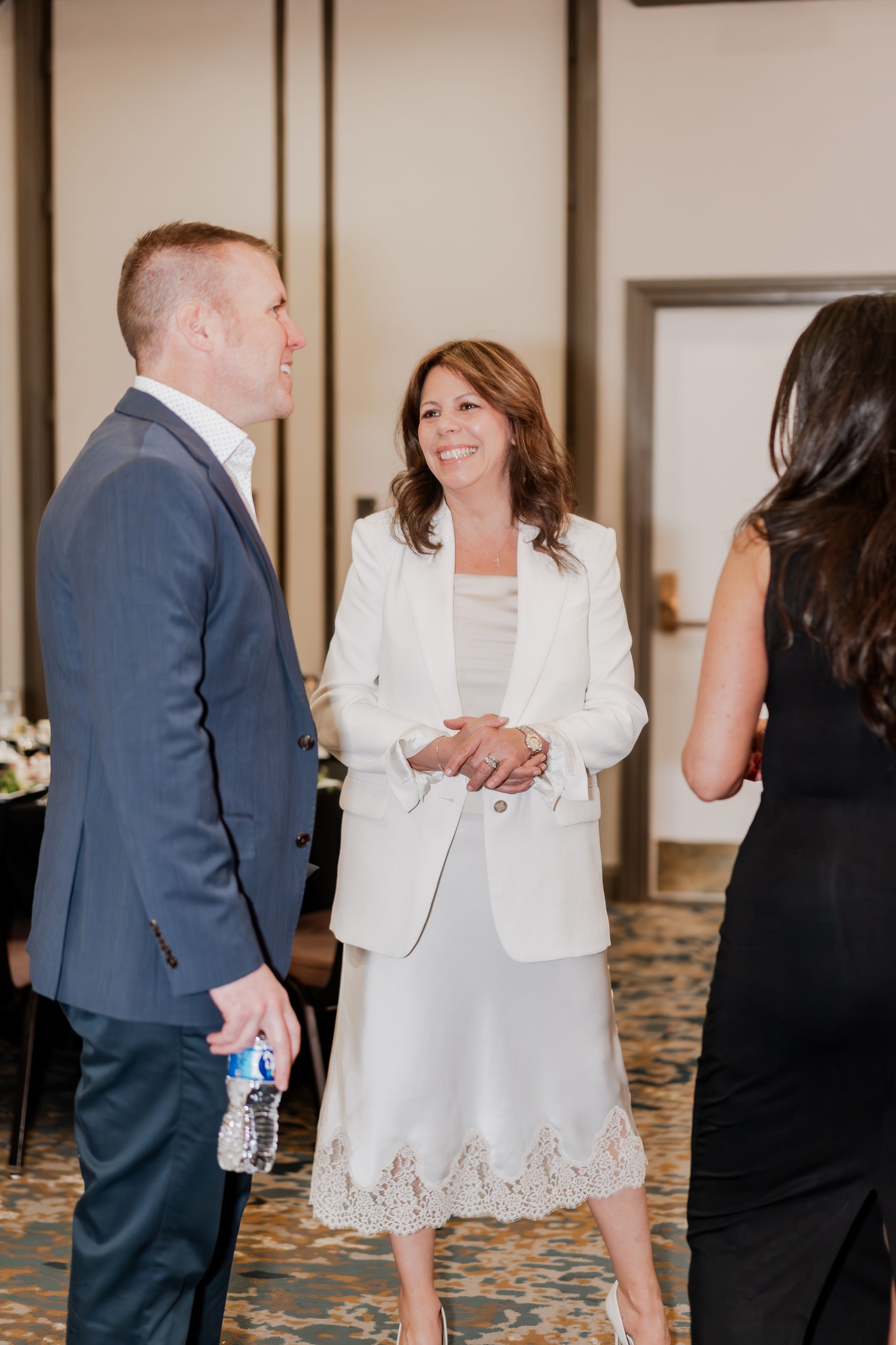 Three people in formal attire stand and converse in a softly lit, carpeted indoor event space.