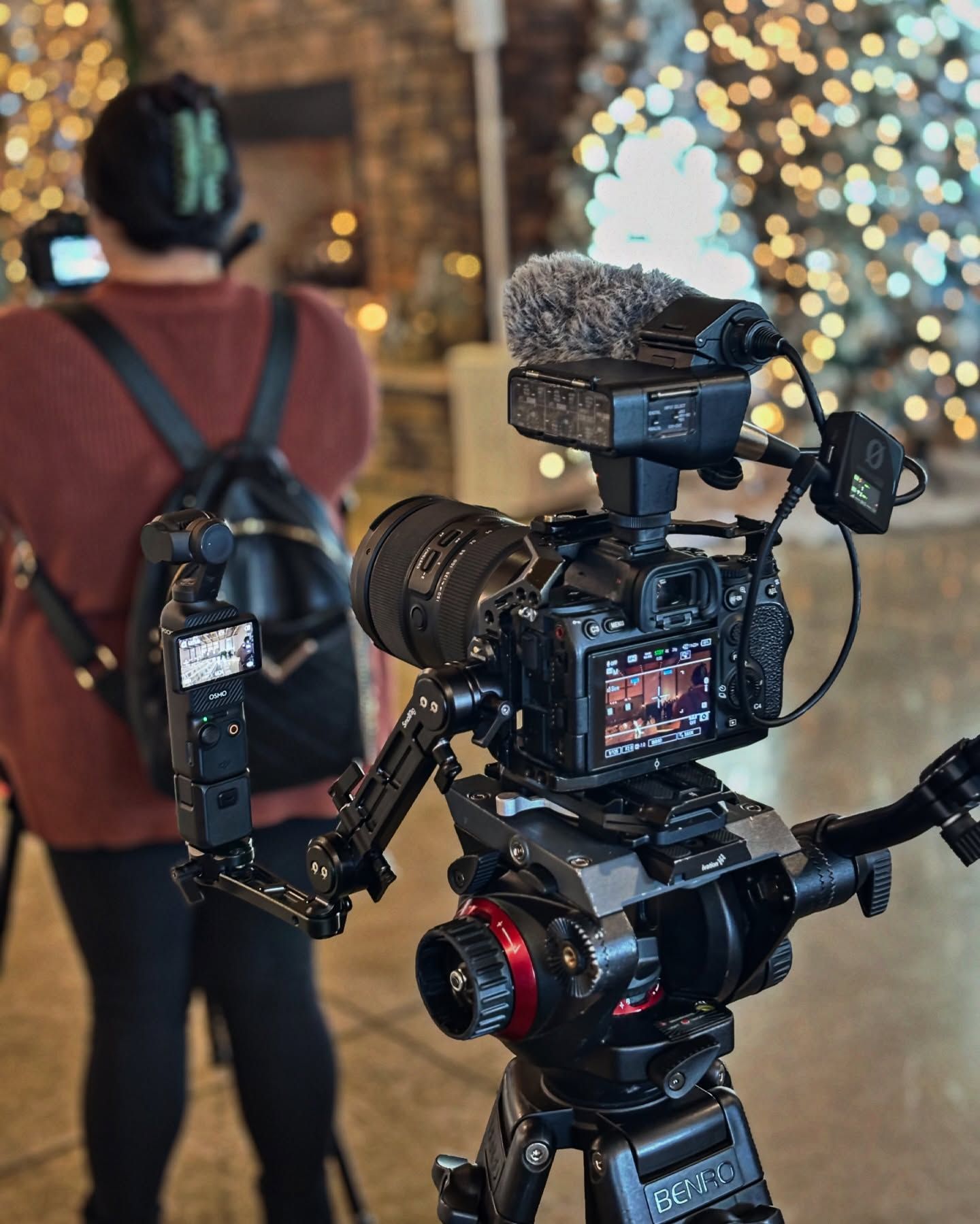 A woman with a backpack is standing in front of a camera on a tripod.