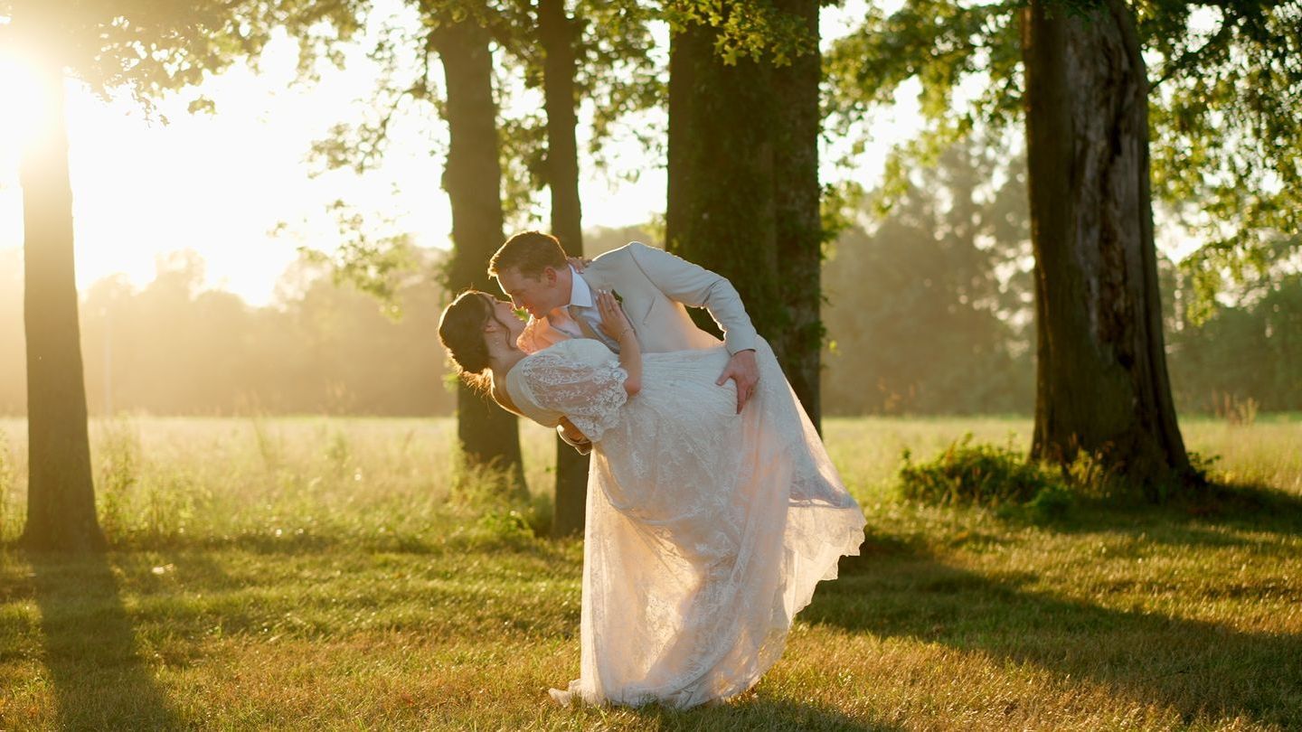 A bride and groom are kissing in a field with trees at Jorgensen Oak Grove