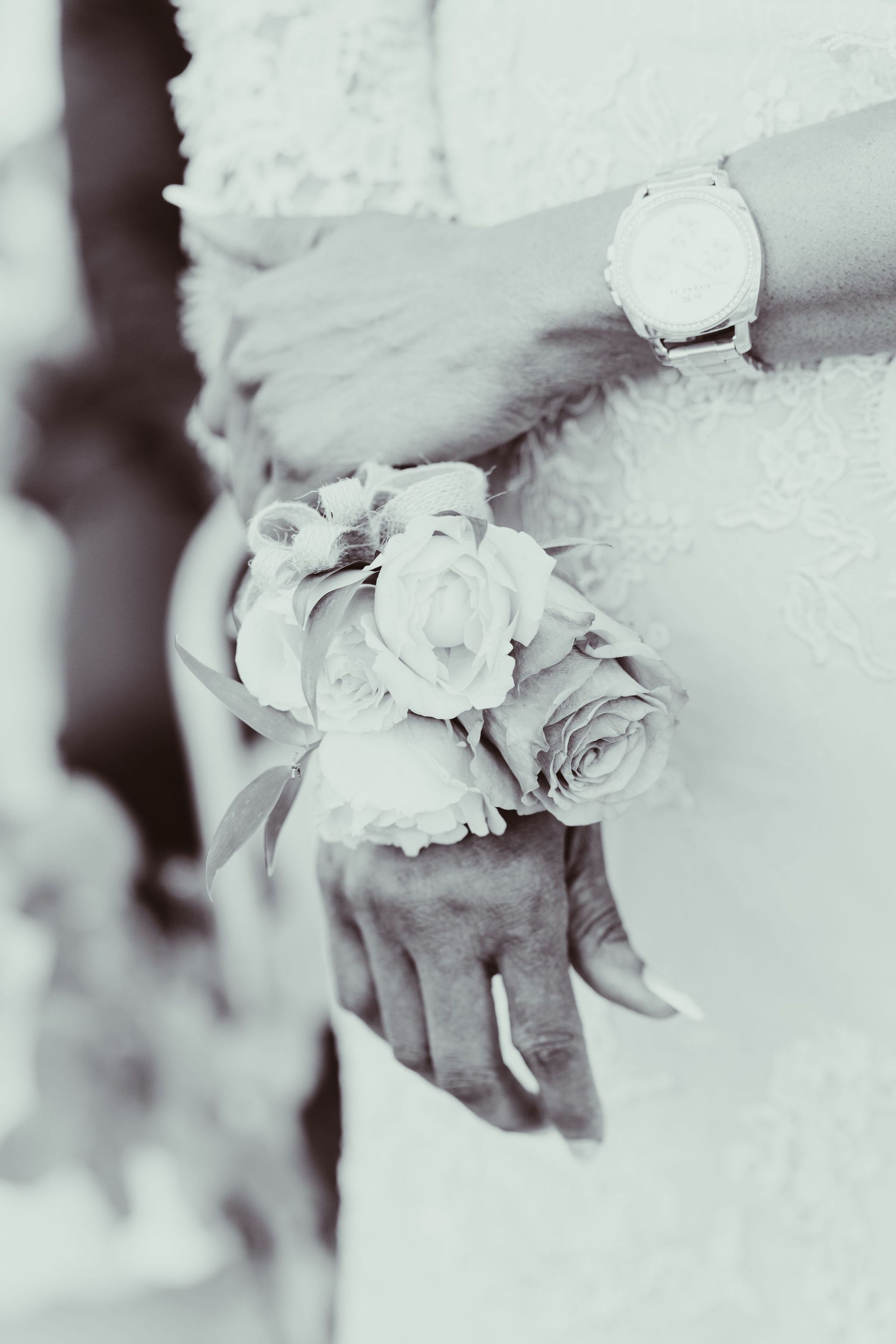 A bride is holding a bouquet of white roses on her wrist.