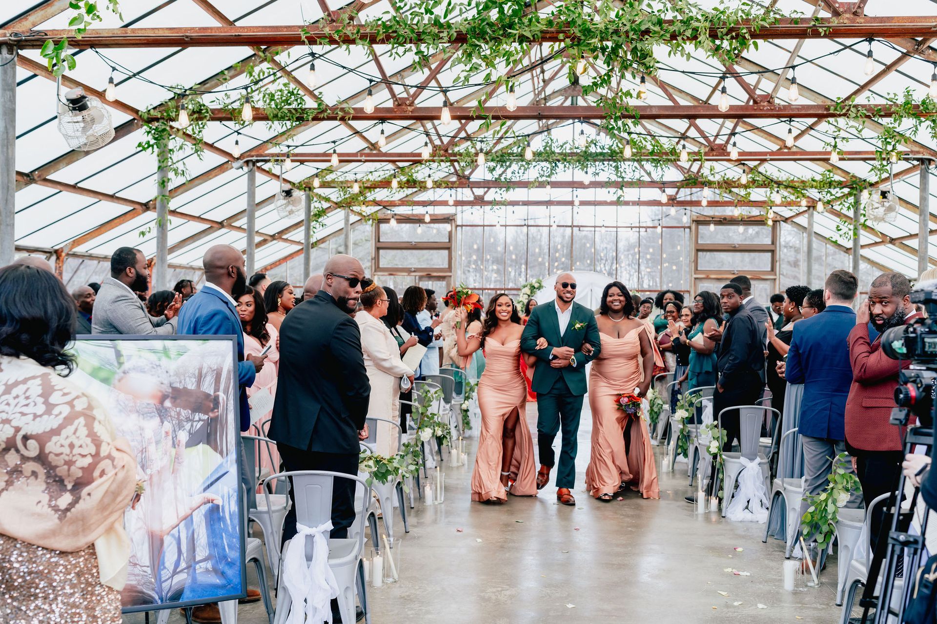 A bride and groom are walking down the aisle at a wedding in a greenhouse.