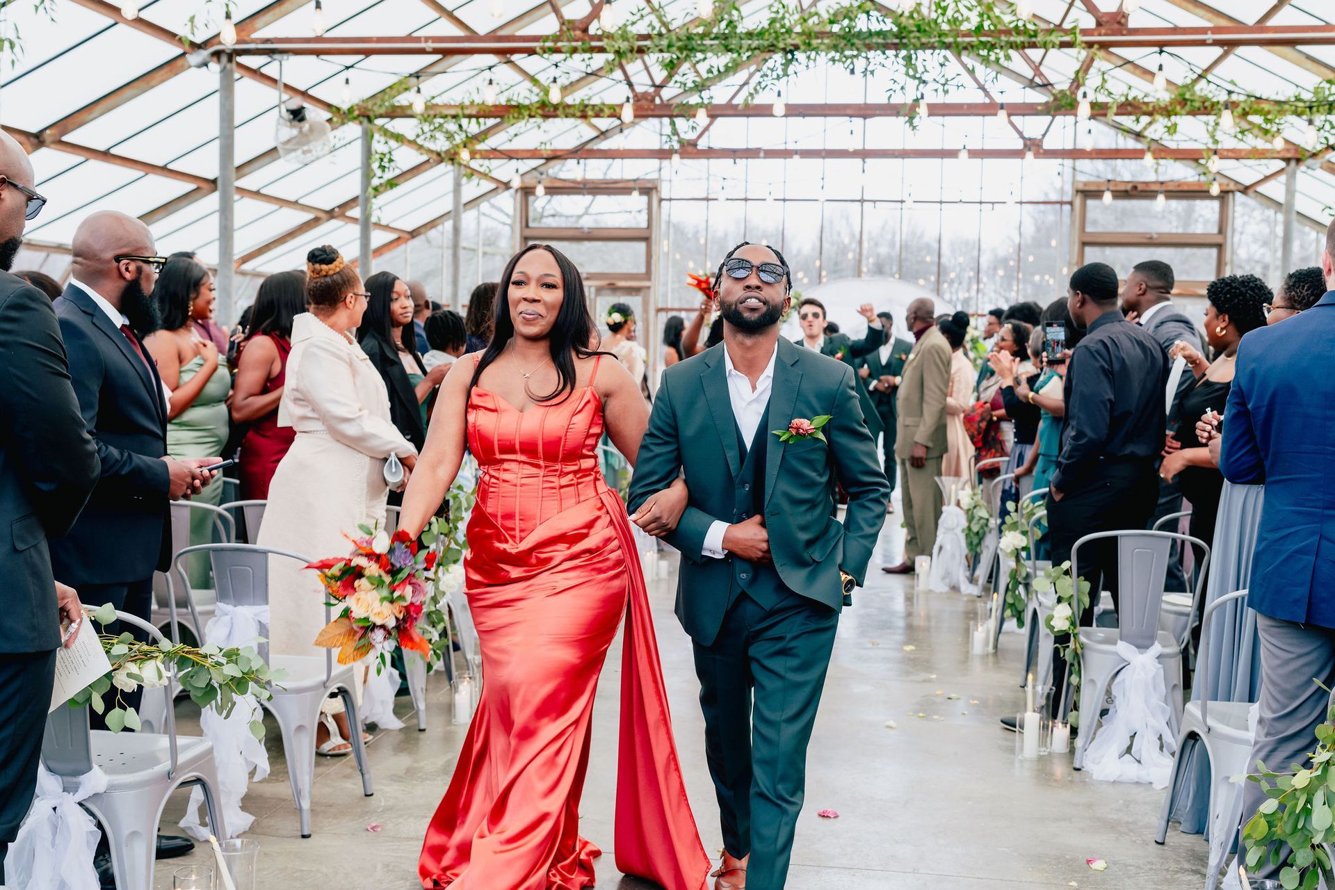 A bride and groom are walking down the aisle at their wedding in a greenhouse.