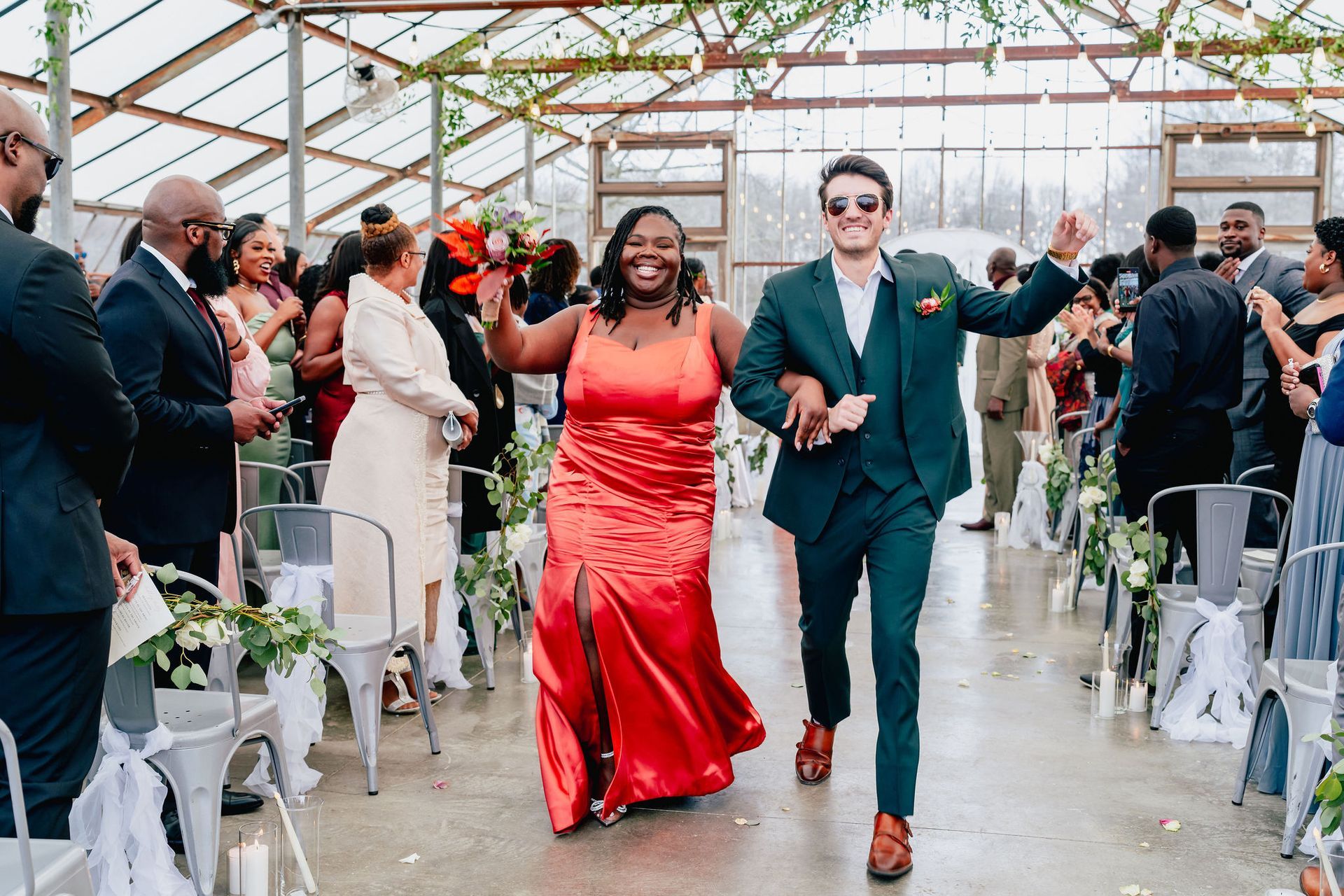 A bride and groom are walking down the aisle at their wedding in a greenhouse.