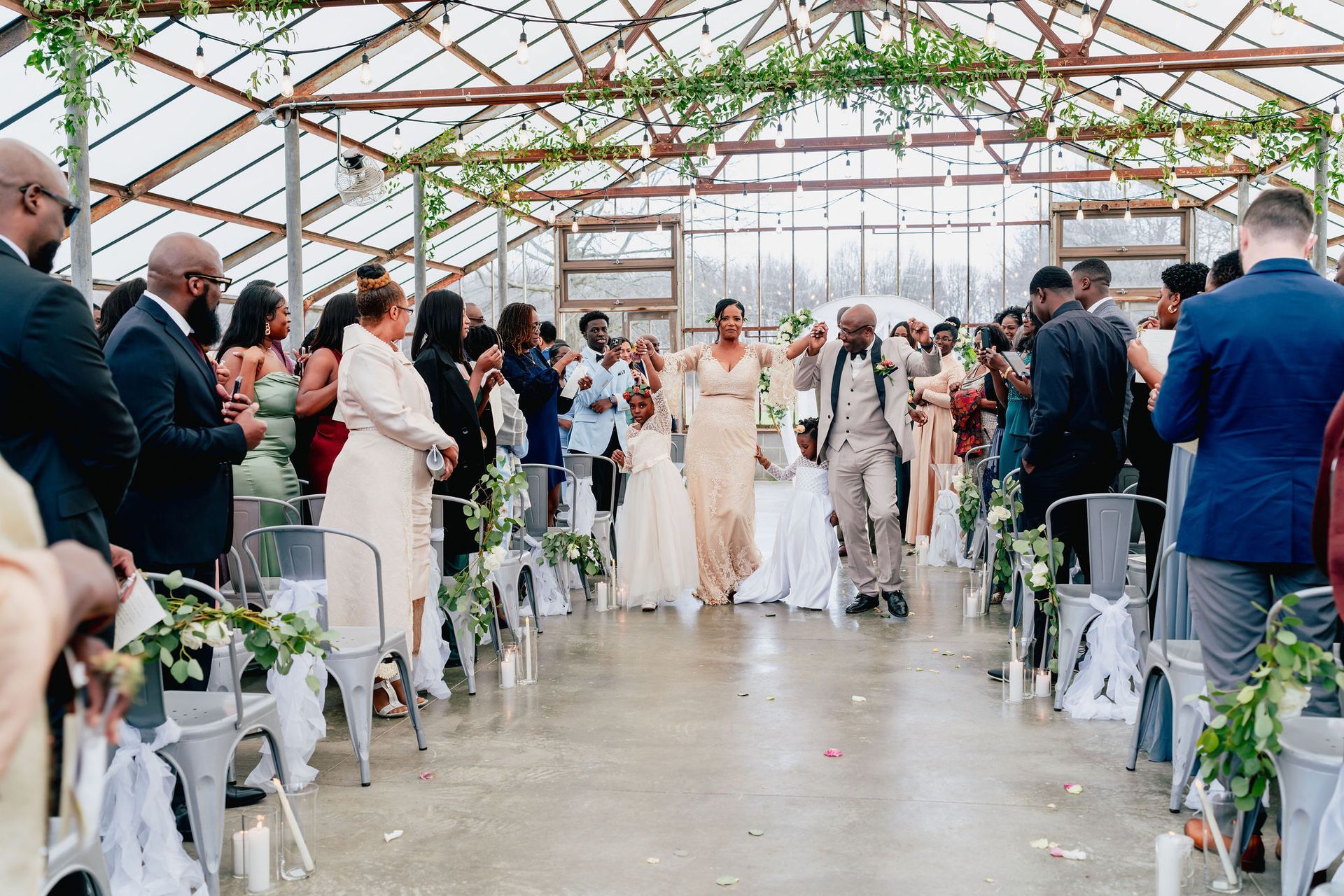 A bride and groom are walking down the aisle at their wedding in a greenhouse.